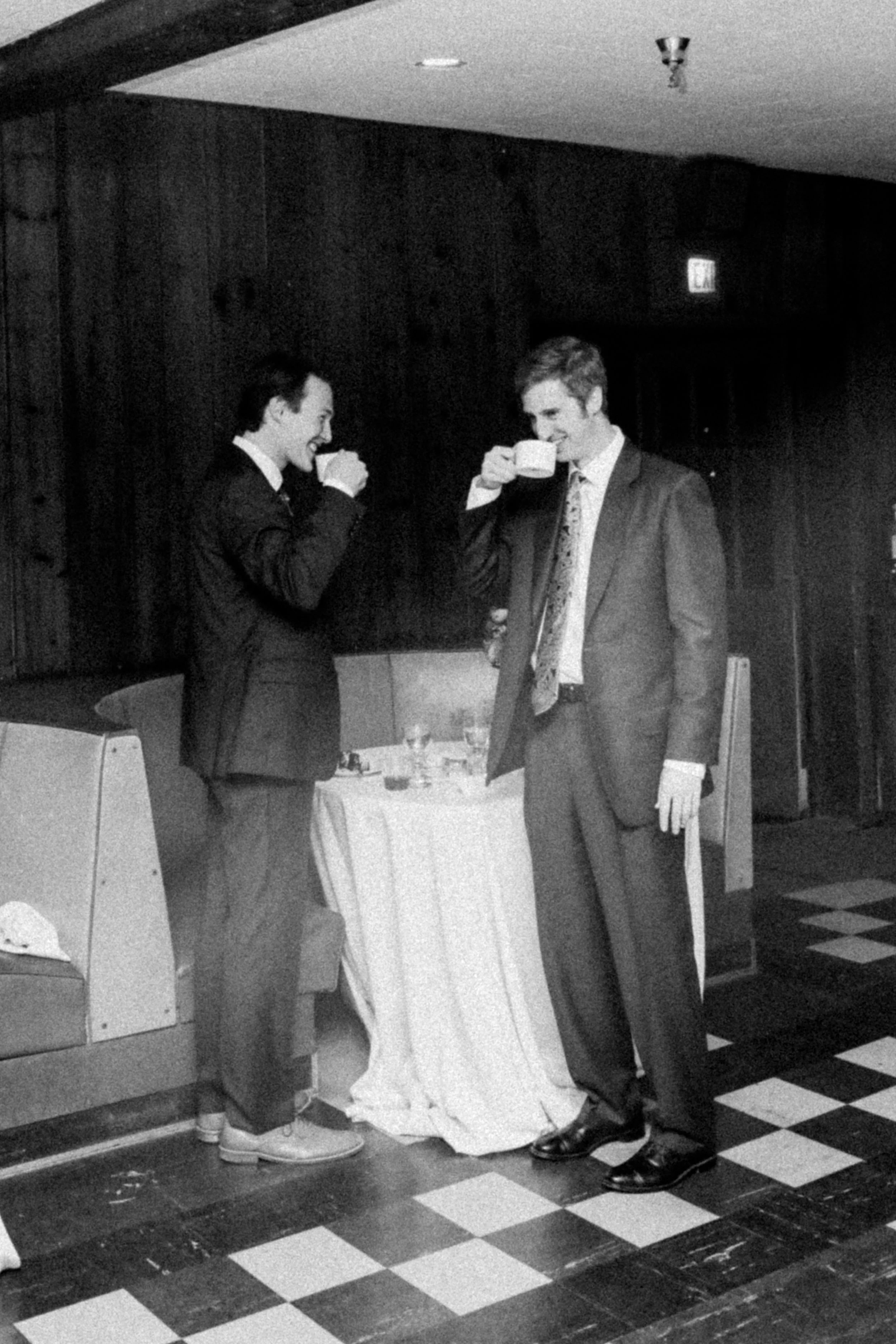 Dos hombres con trajes de negocios toman café en un restaurante, uno de ellos sonríe.