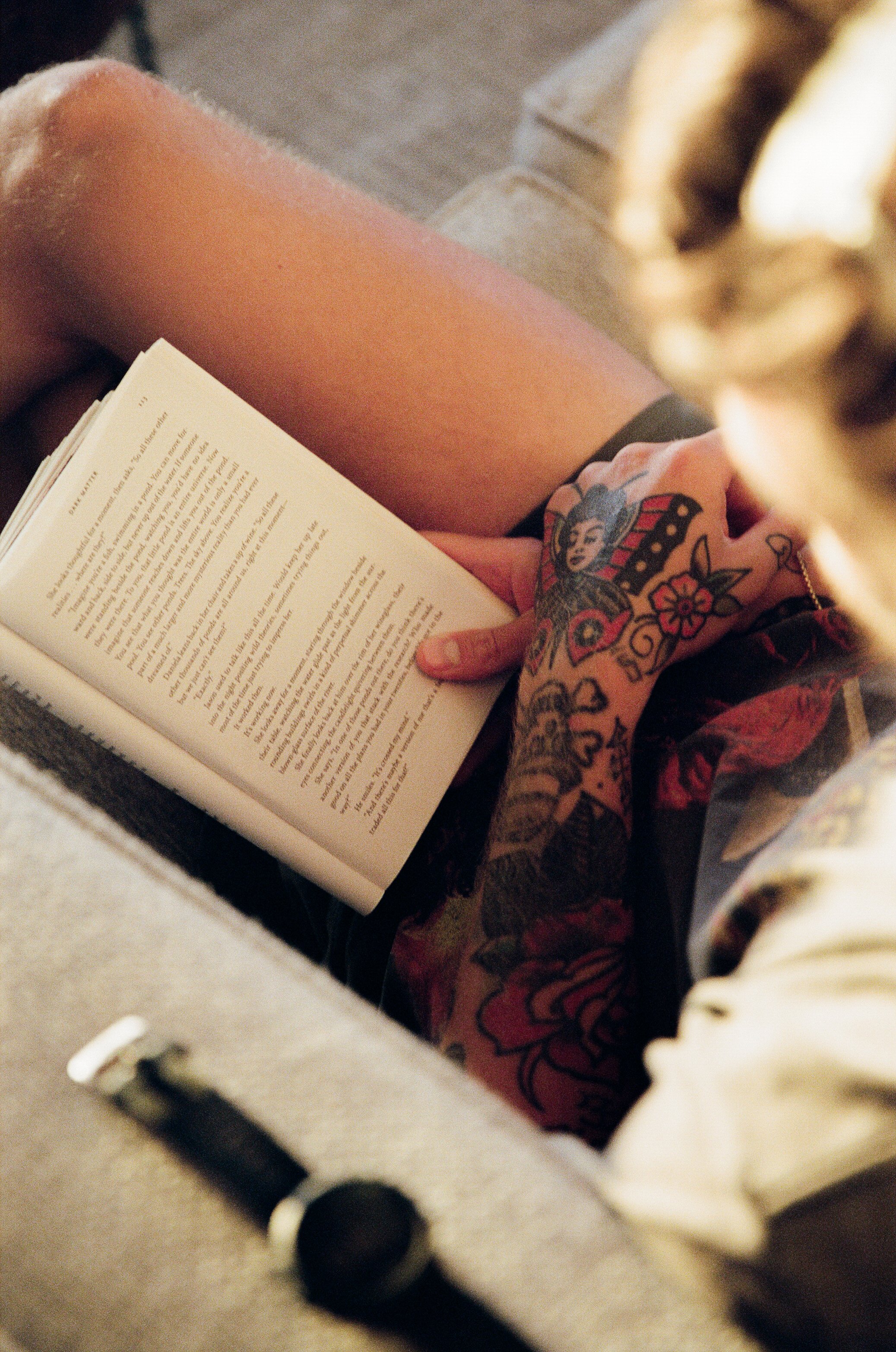 Una persona con tatuajes en la mano leyendo un libro en un ambiente cómodo.