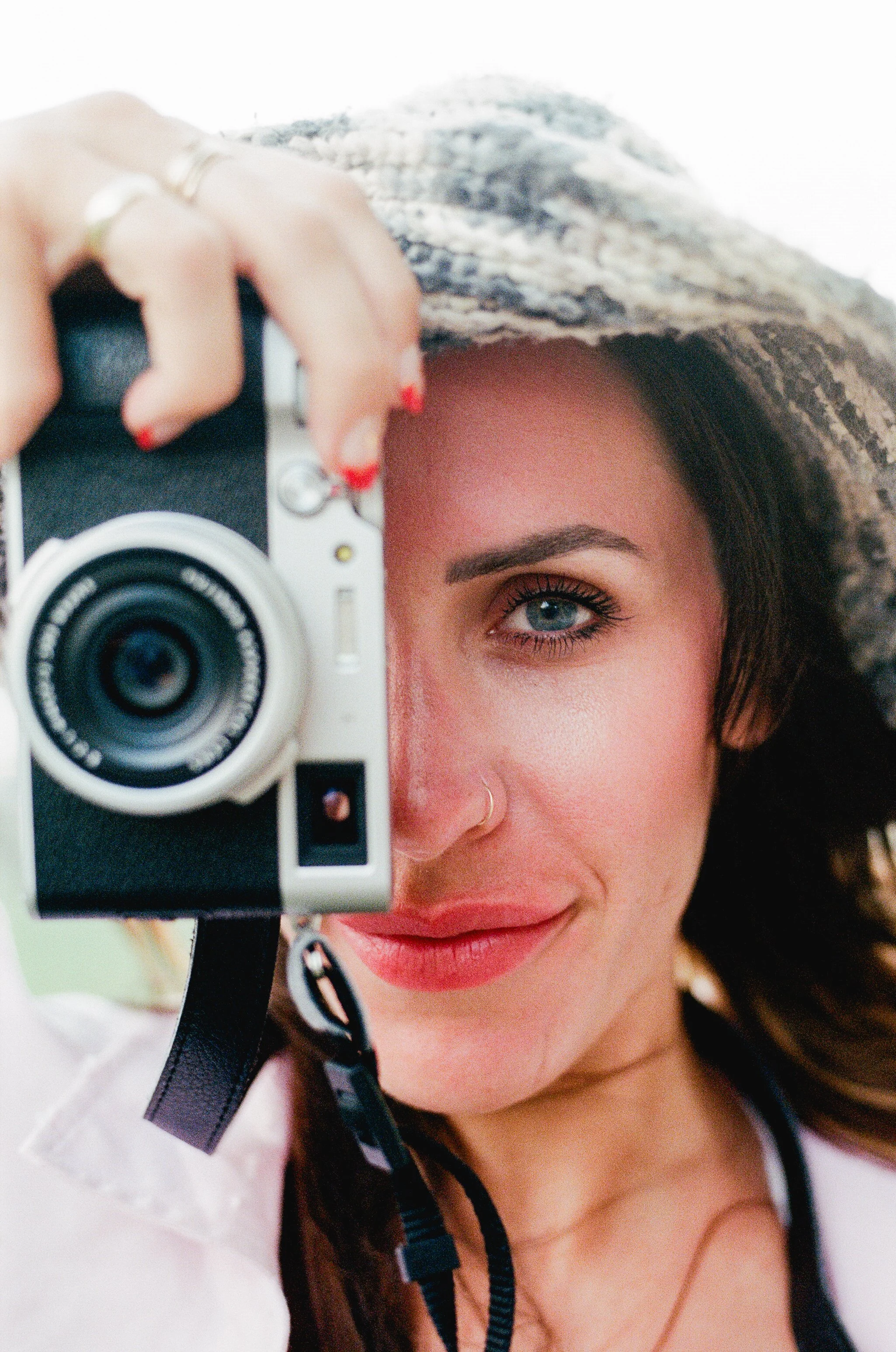 Mujer con sombrero tomando una selfie con una cámara en primer plano, enfocada en su rostro y ojo.