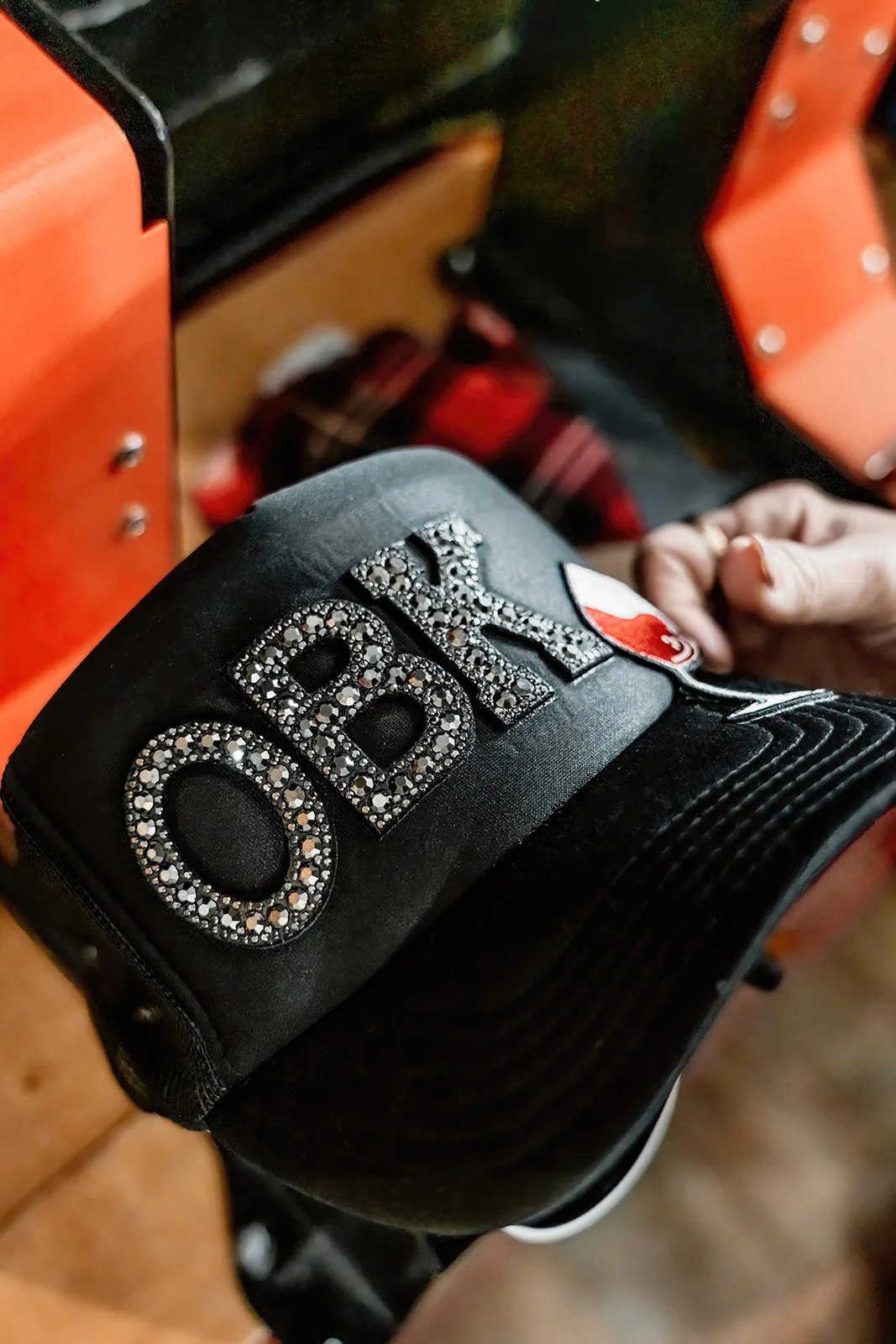Close-up of a black hockey glove with the word 'OBI' written in rhinestones, held by a person's hand.