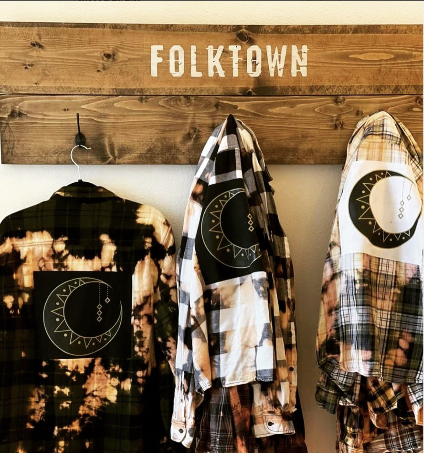 Three flannel shirts hanging on a wall with a wooden sign that says "FOLKTOWN" above them.