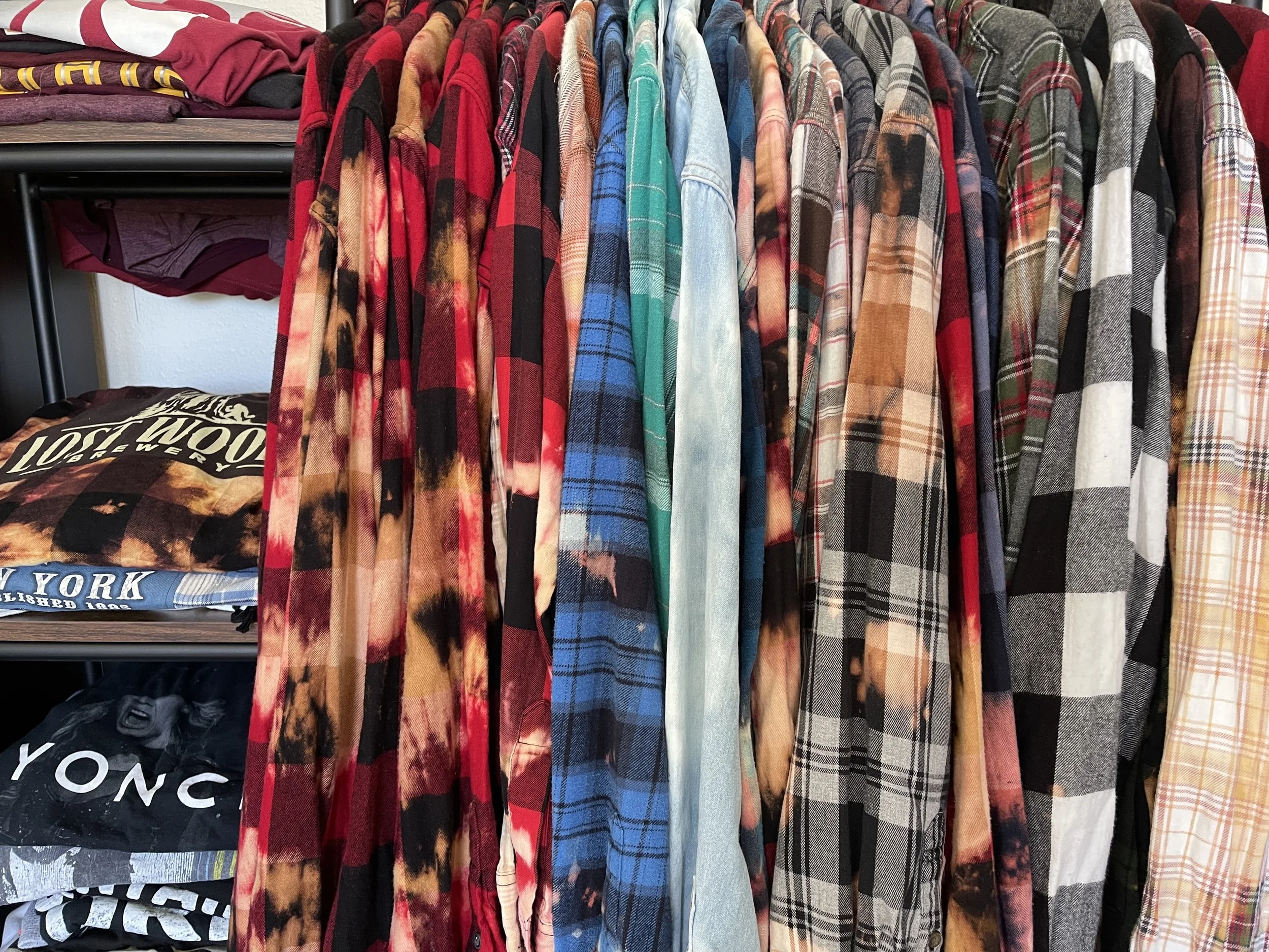 A rack of plaid and tie-dye shirts in various colors including red, blue, green, yellow, and black, hanging next to each other.