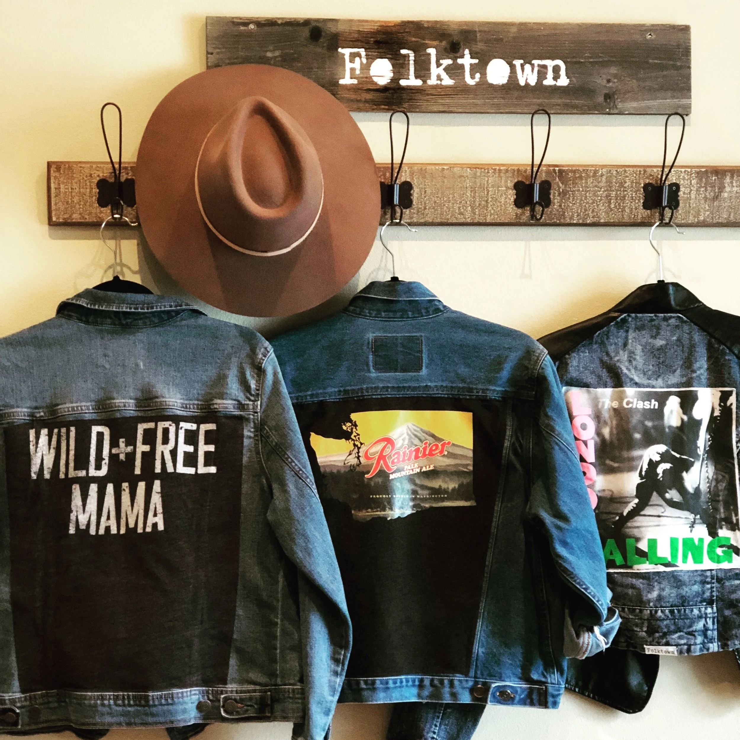 Custom upcycled denim jackets with patches hanging on hooks beneath a wooden sign that says 'Folk town' and a hat hanging on a hook.