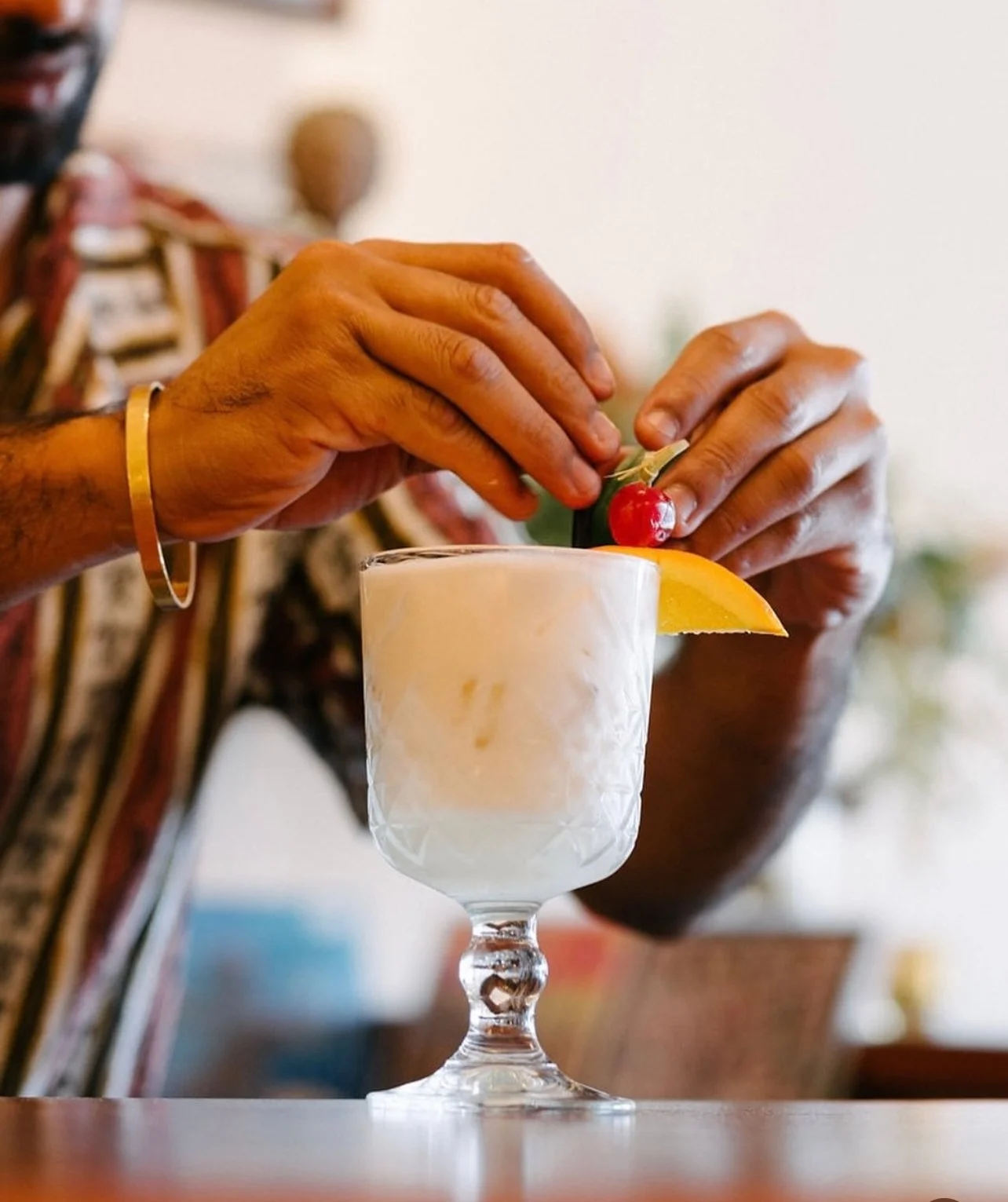 Hands garnish a tropical cocktail with a cherry and lemon slice.