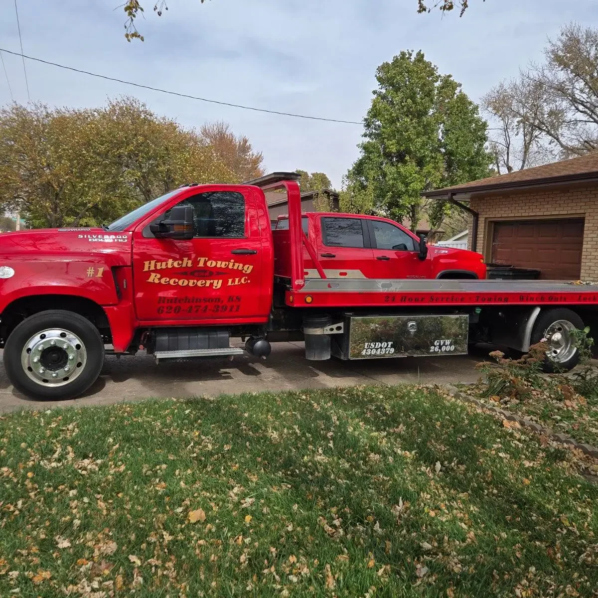 Red tow truck parked in front of a house with a red pickup truck loaded onto its bed.