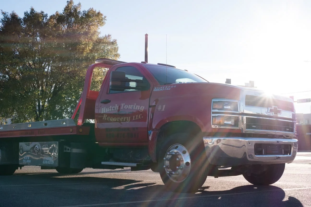 Red tow truck with 'Hatch Towing Recovery LLC' written on the side, parked outdoors with sunlight shining and trees in the background.