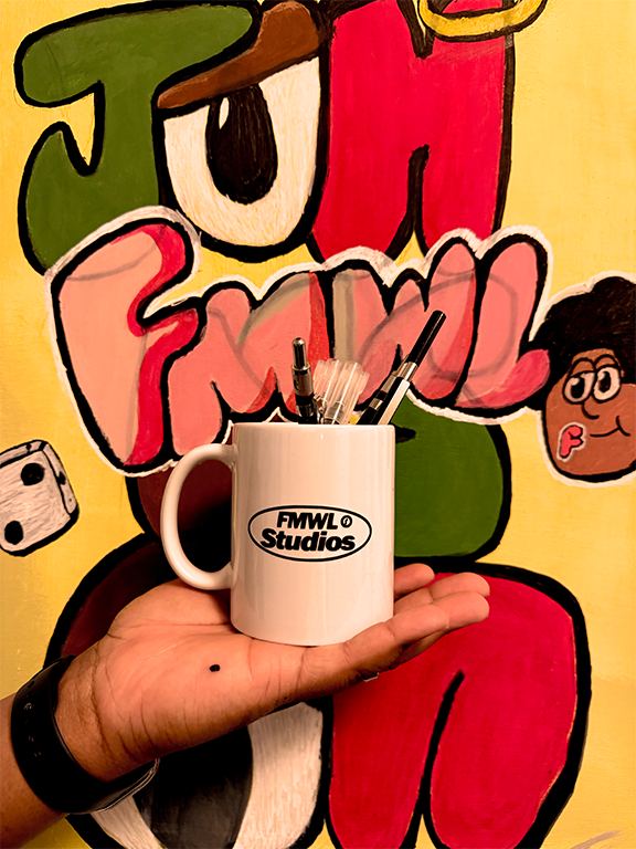 A person holding a white mug with the logo 'FMWL Studios' in front of a colorful graffiti-style mural with various characters, including a cartoon face, a camera, and stylized text, on a bright yellow background.