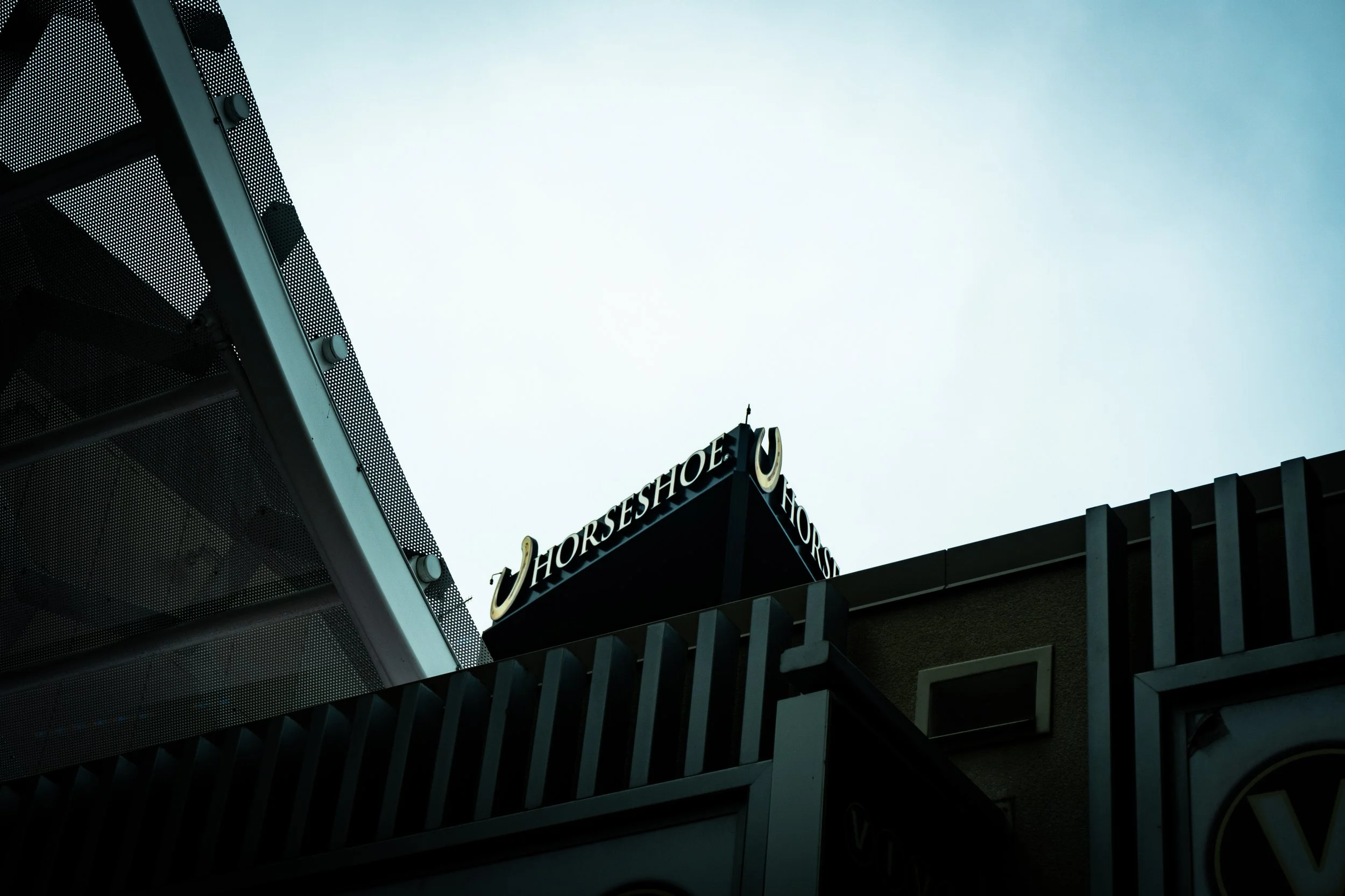 Low-angle view of a building with a sign that reads 'Horseshoe Lounge' in black letters on a black background, against a cloudy sky.