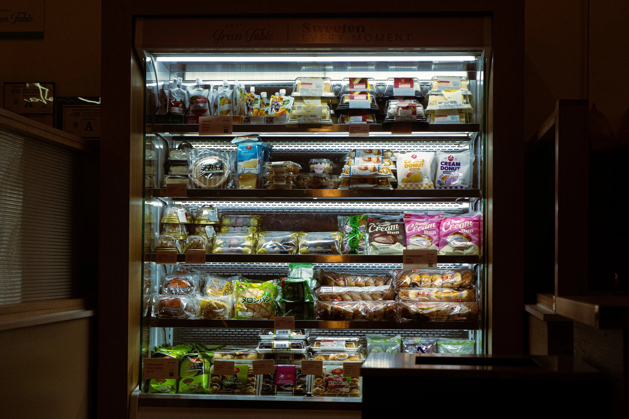 A refrigerator filled with various packaged baked goods, including cakes, donuts, and buns, in a grocery store aisle.