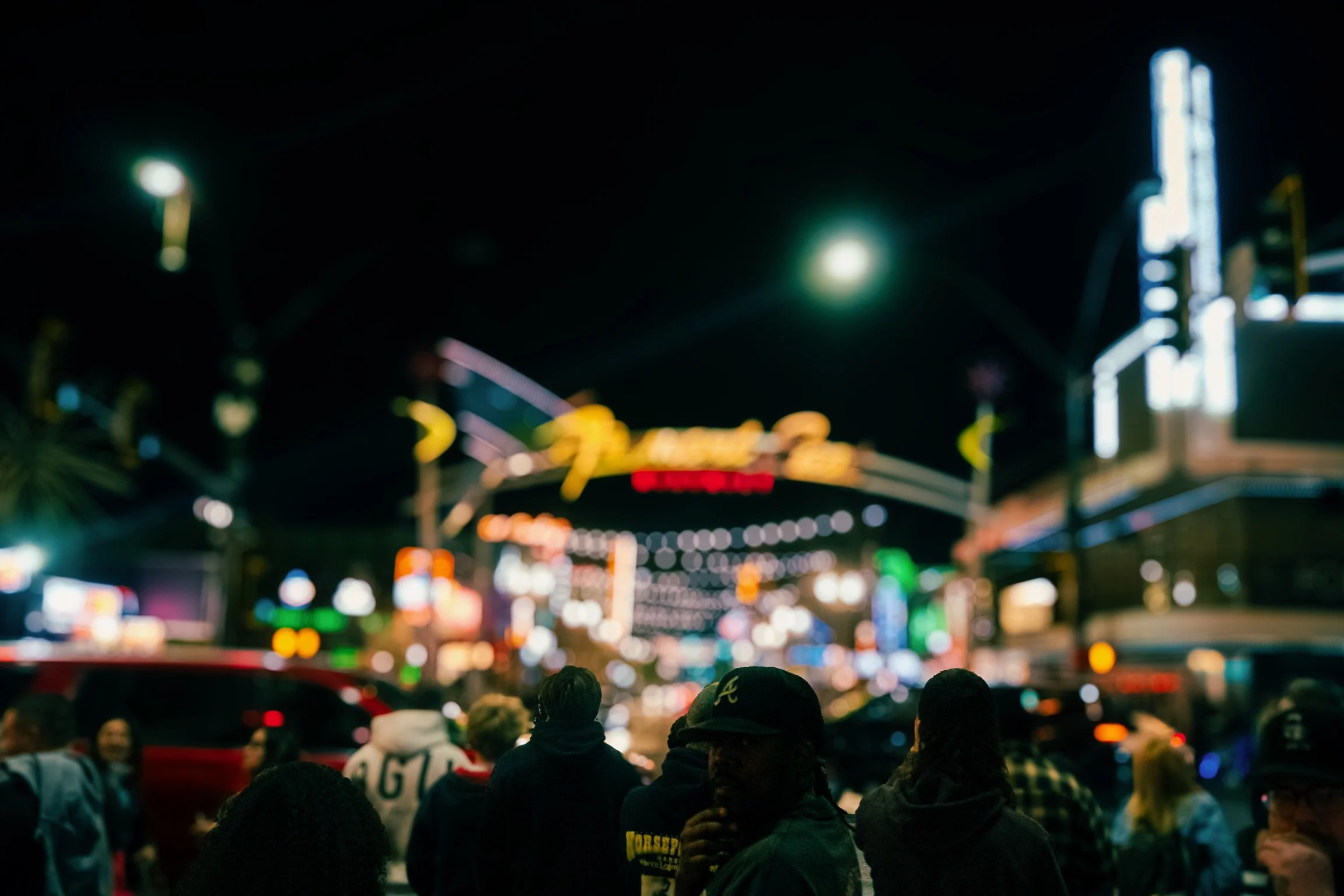 Night scene of a city street filled with people, brightly lit signs, and blurred neon lights in the background.