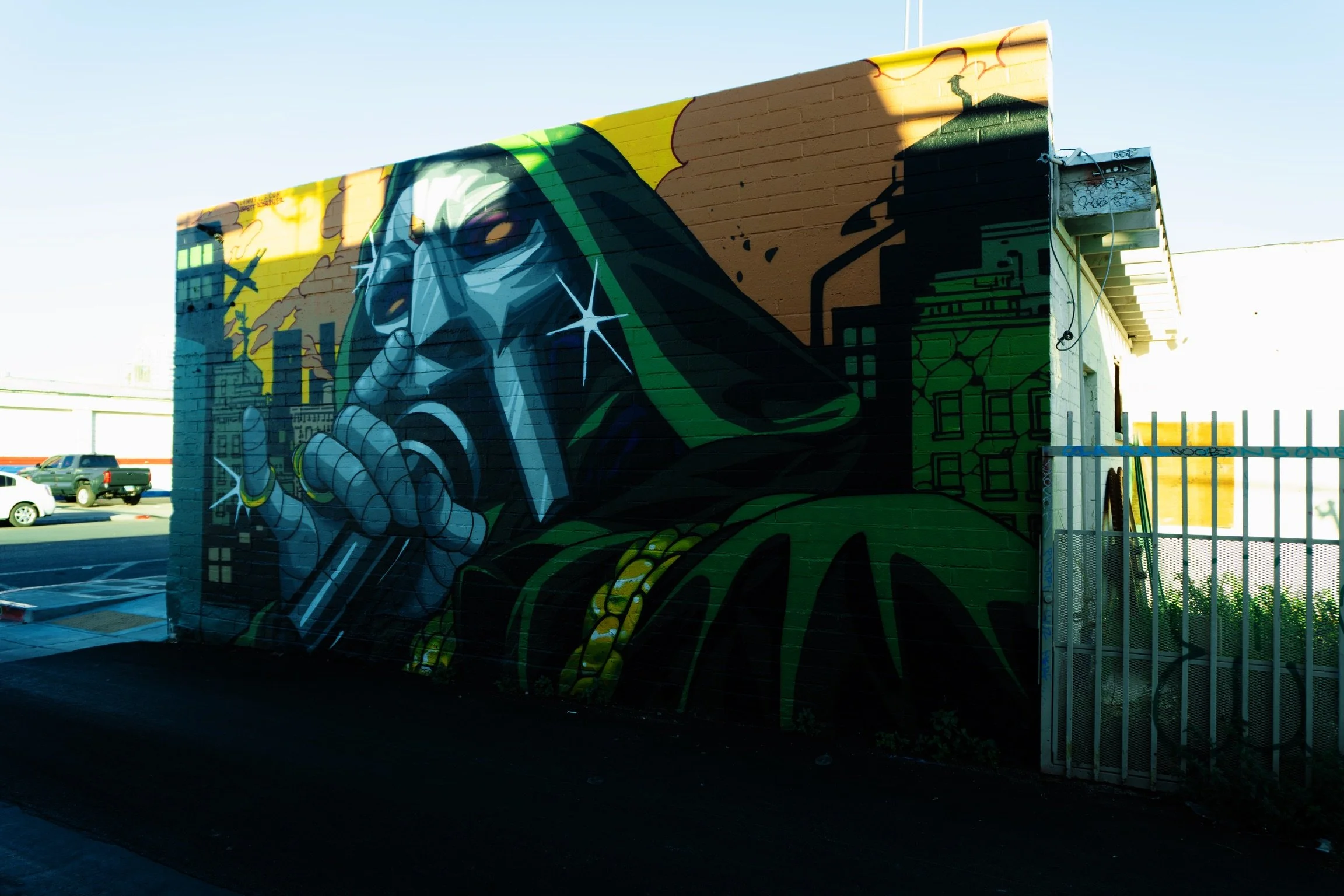 Street mural of a rapper with sunglasses, holding a microphone, cityscape background, in graffiti art style.