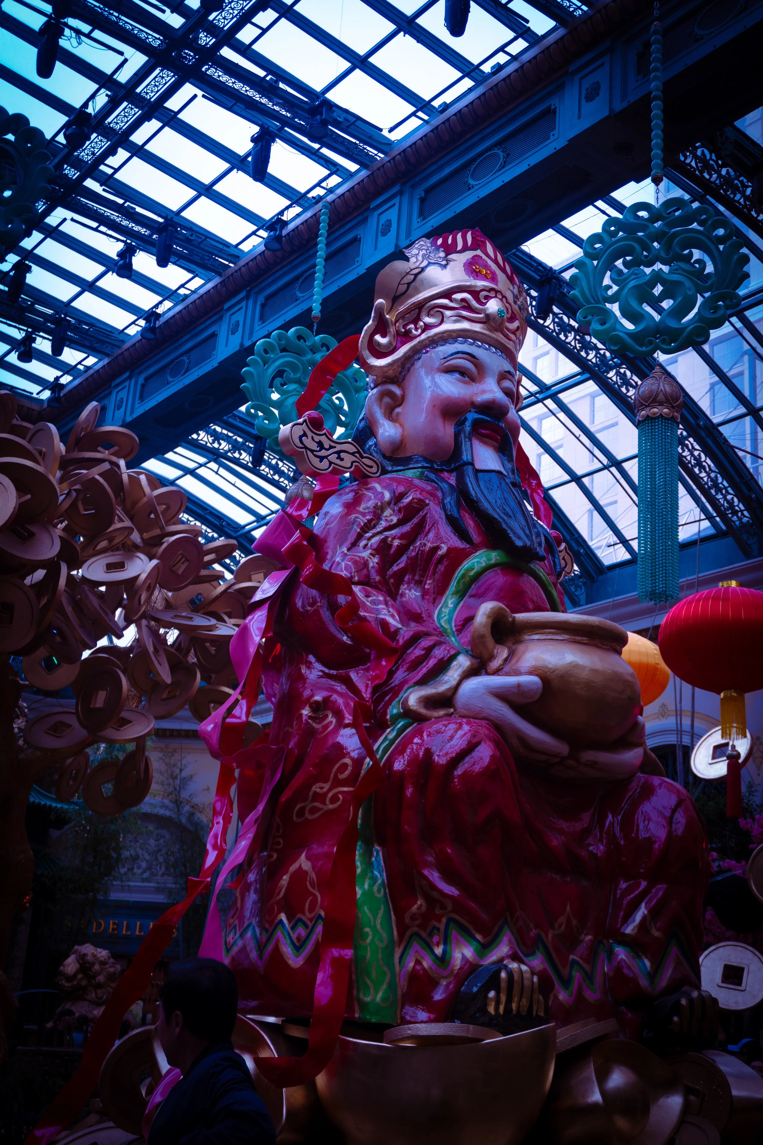 Large colorful statue of a Chinese god or deity inside a glass-roofed indoor space decorated with lanterns and traditional ornaments.
