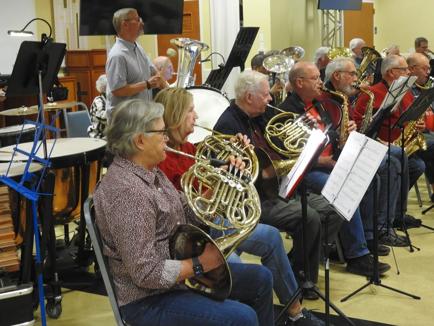 Adults playing french horns and percussion at a rehearsal of New Horizons Band Austin Texas