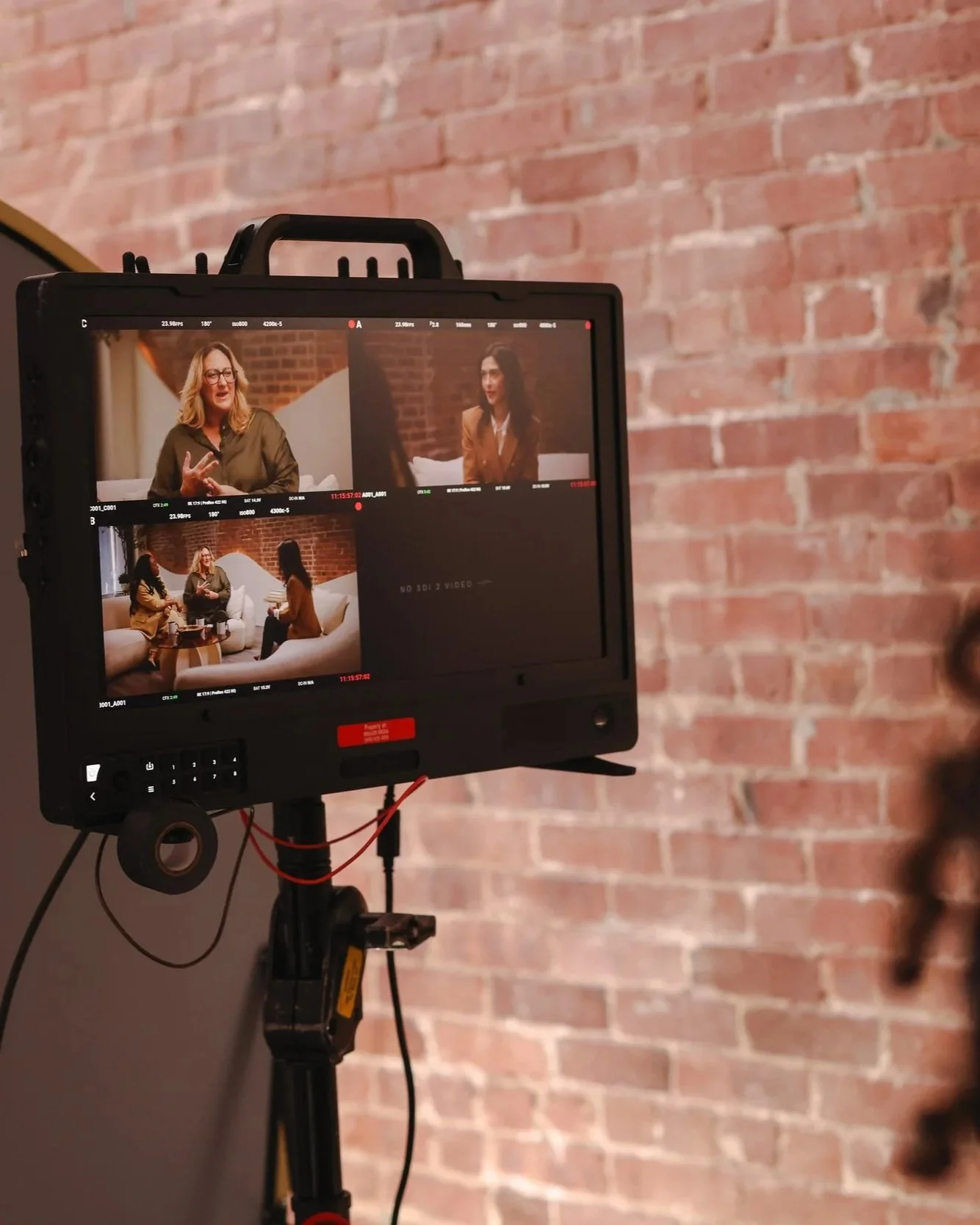 Video camera monitor shows scenes of three women sitting and talking in a brick-walled room.