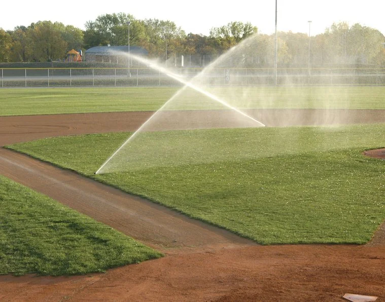 A baseball field with sprinklers watering the grass.