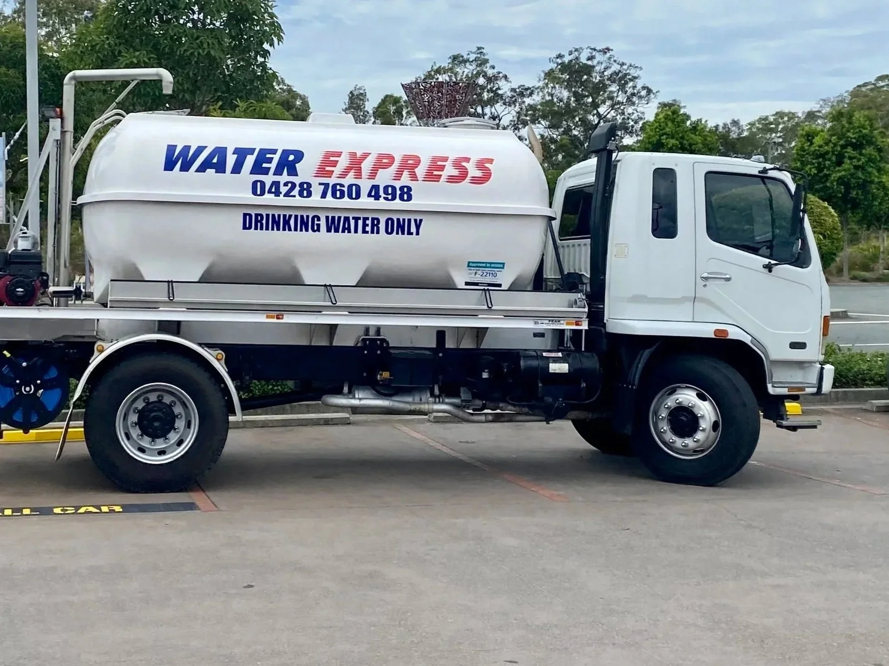 White water delivery truck with a large tank labeled 'Water Express' and 'Drinking Water Only' parked in a lot with trees in the background.