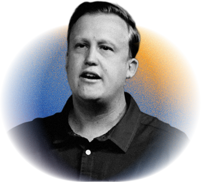 A young man with short hair, wearing a dark shirt, speaking with a serious expression, in front of a background with a large curved gradient of blue and yellow colors.