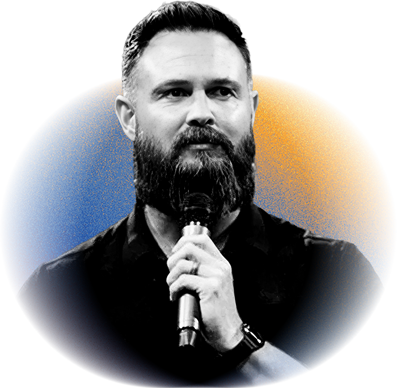 A man with a beard and short hair holding a microphone while speaking.