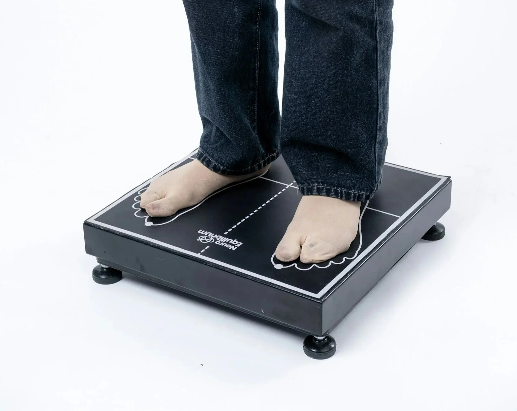 Person standing on a black Landau Equilibrium balance platform, wearing socks and jeans, with the platform marked with white lines and markings.