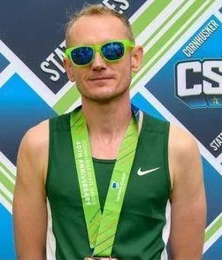 Athlete wearing green sunglasses and a green Nike sports top with a medal around his neck at a road race event.