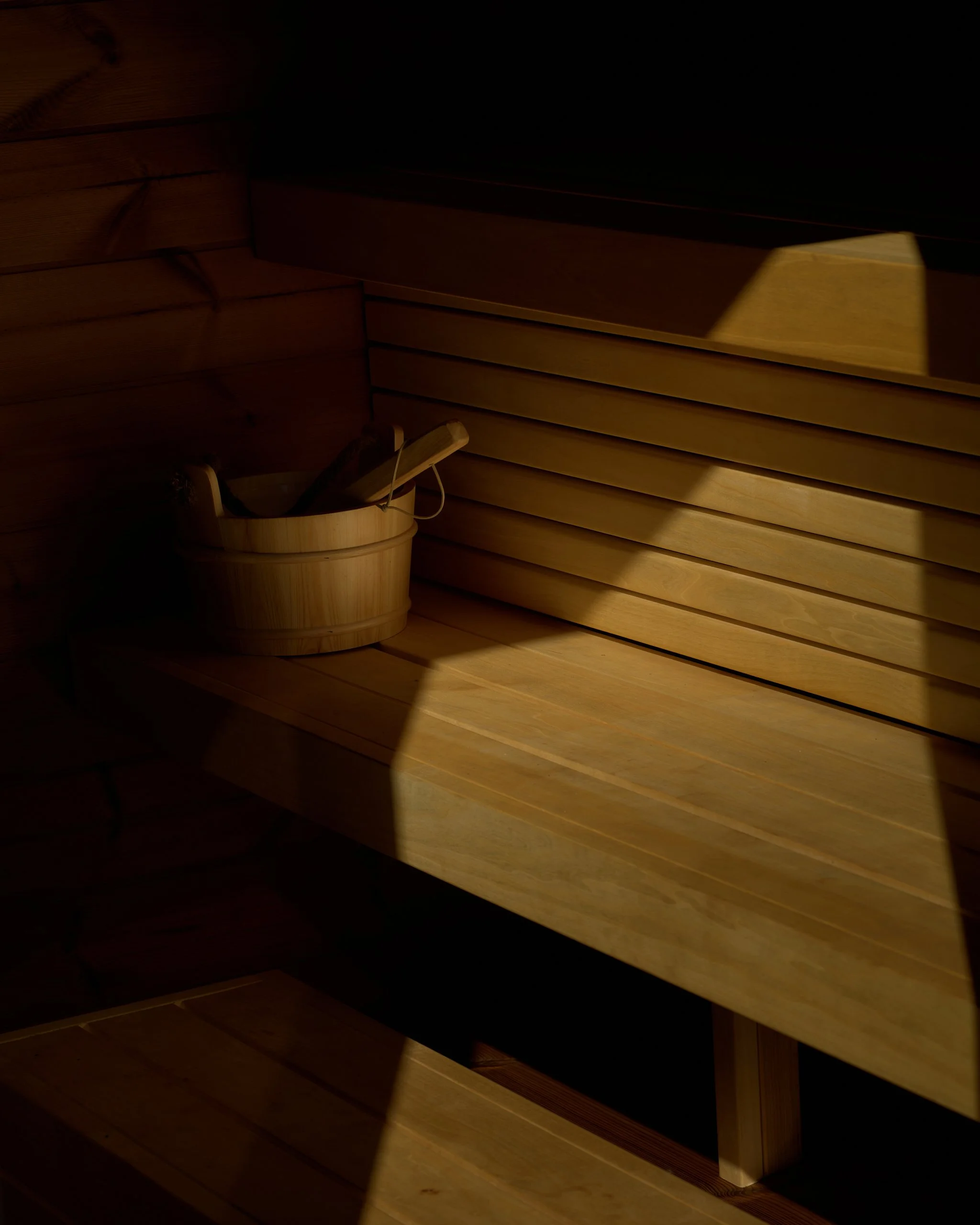 Interior view of a wooden sauna with horizontal wood paneling and a wooden bucket with a ladle inside.