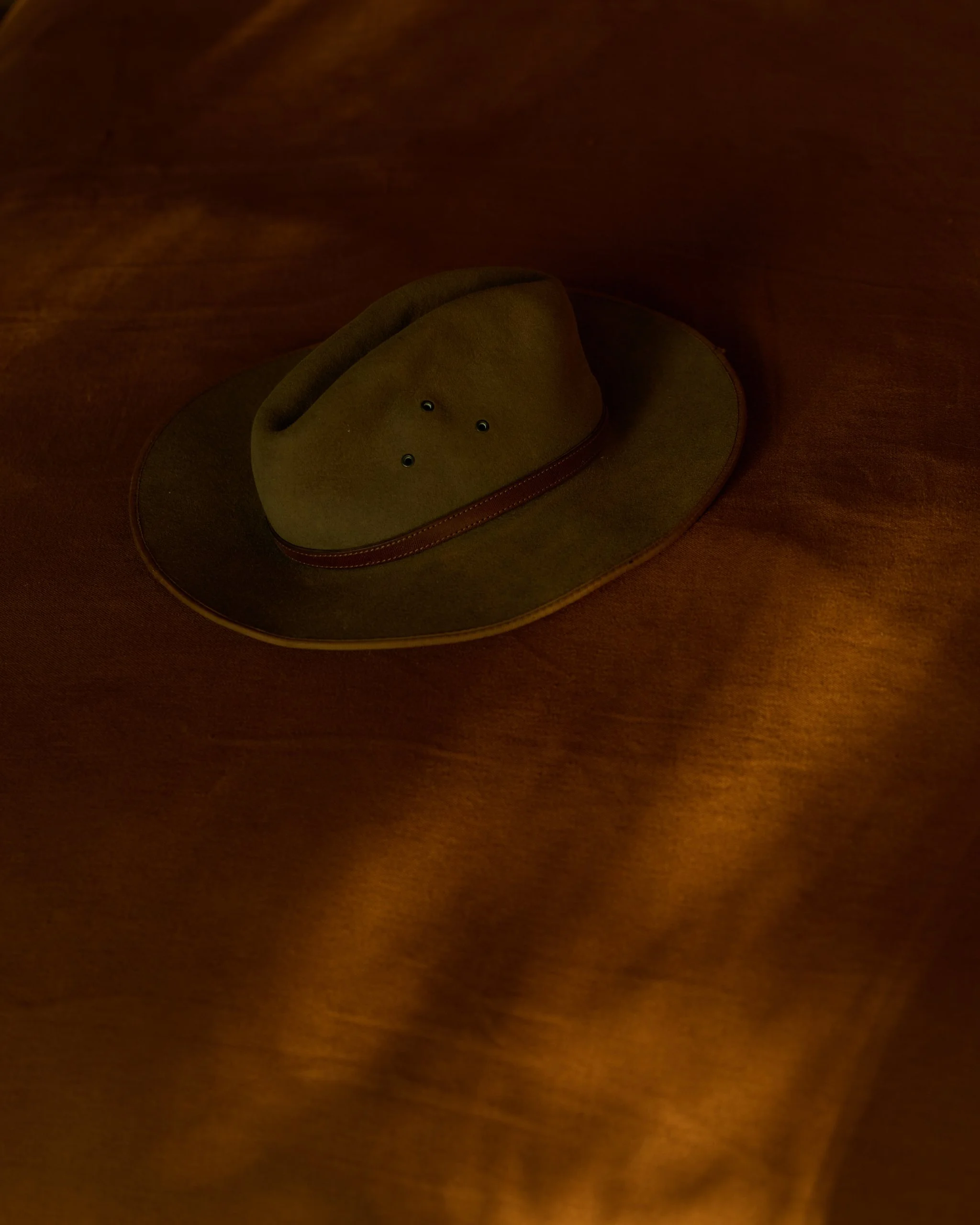 A brown cowboy hat, with a red band, resting on a wooden surface.