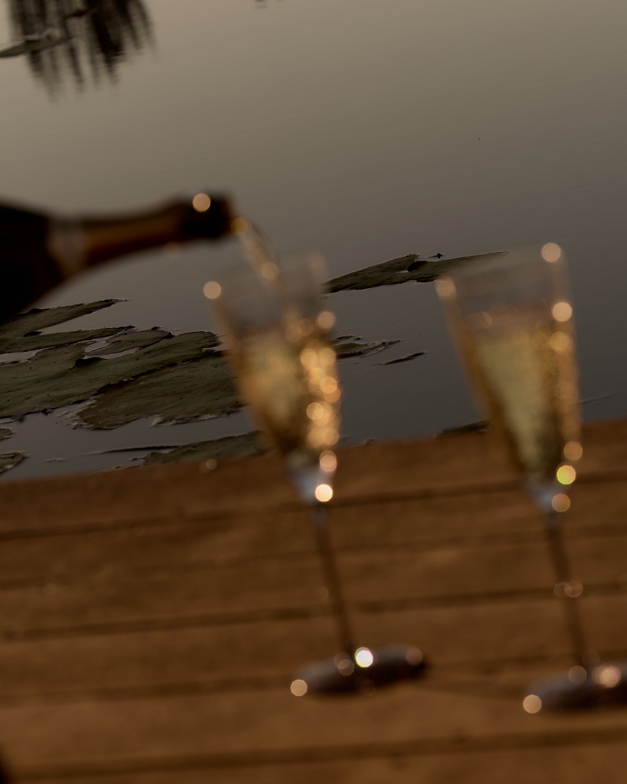 Blurred image showing a close-up of a glass of beer with bubbles, a water surface with reflections, and some rocks or islands in the background.