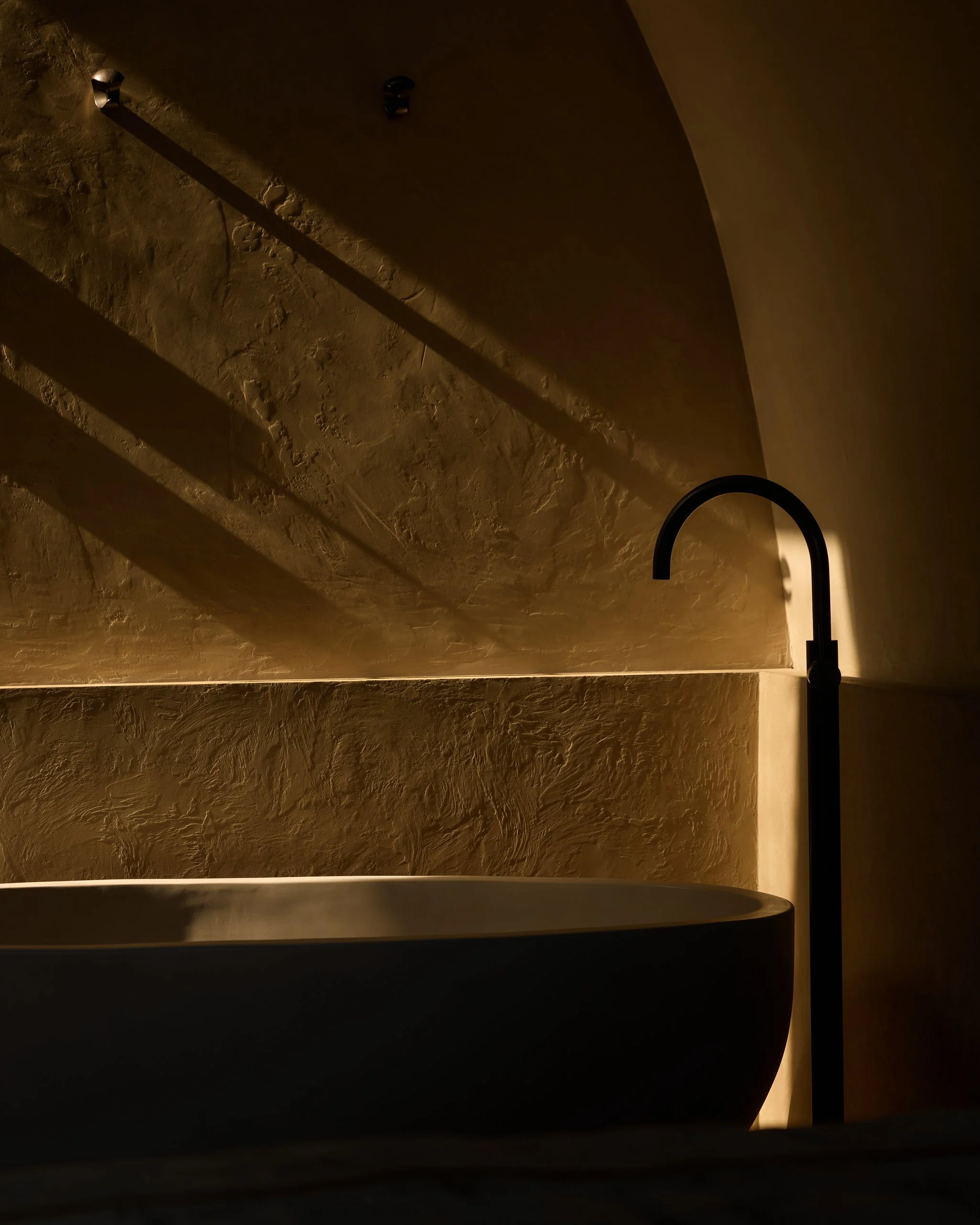 Close-up of an interior with textured walls, soft lighting, a black curved object in the foreground, and a black faucet on the right side.