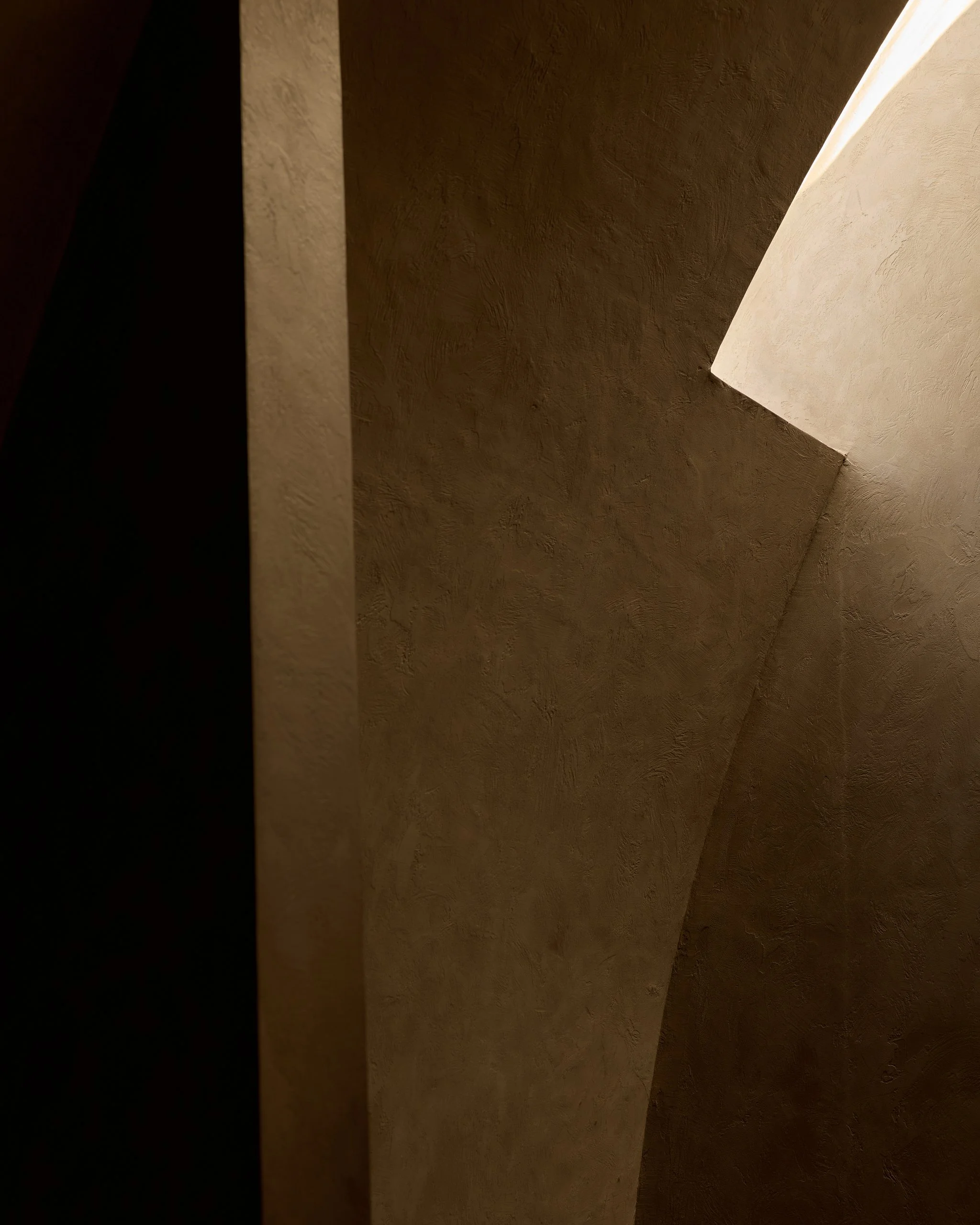 Close-up of textured ceiling and walls with forms and shadows, highlighting different shades of beige and brown.