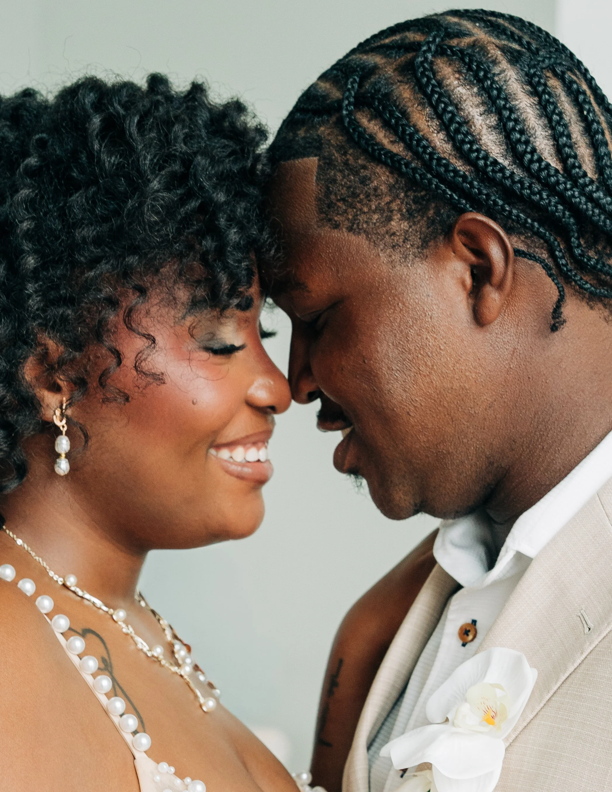 Close-up of bride and groom touching foreheads, both smiling, with visible bracelets and orchid boutonniere on groom's lapel. Photography and Wedding content creation on the Eastern Shore.