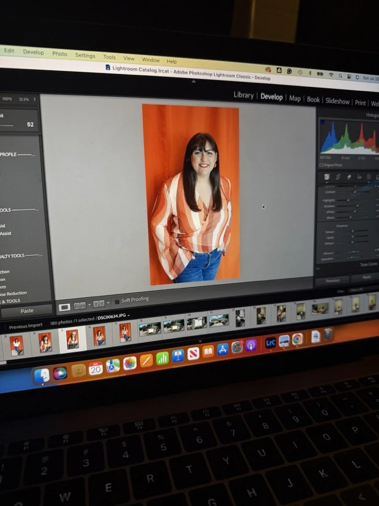 A woman with dark hair and bangs wearing a vertically striped orange and white blouse, standing in front of an orange background, displayed on a computer screen in Adobe Photoshop Lightroom.