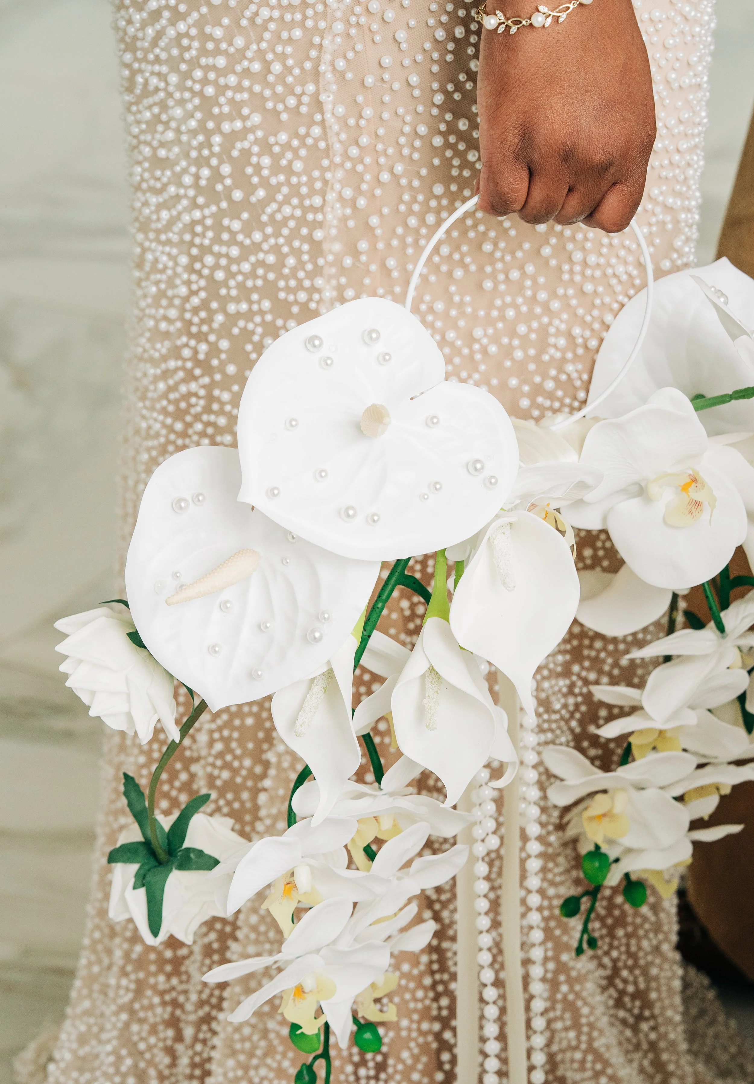 A person wearing a beige dress with white pearl-like embellishments holding a white orchid flower with pearl decorations in their hand. Second Shooting for Wedding Photographers along the Gulf Coast.