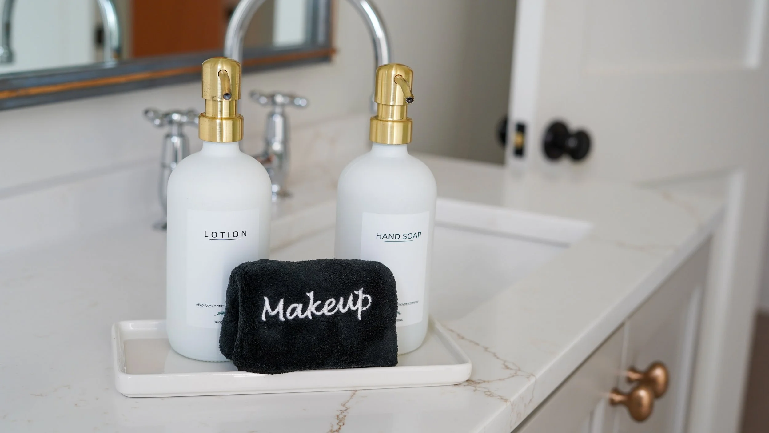 White bottles labeled lotion and hand soap on a bathroom counter with a black makeup towel and a mirror in the background. Social media manager in Fairhope documenting photos for client to use on social media.