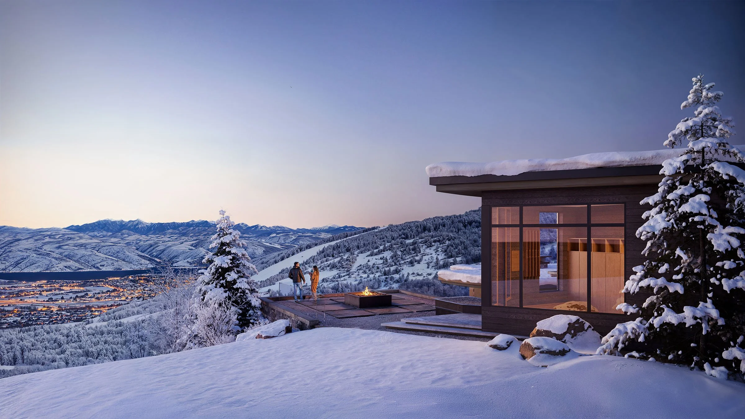 A modern house with large glass windows on a snow-covered hillside, overlooking a valley and mountain range during twilight, with two people standing on the deck near a fire pit and snow-covered trees.