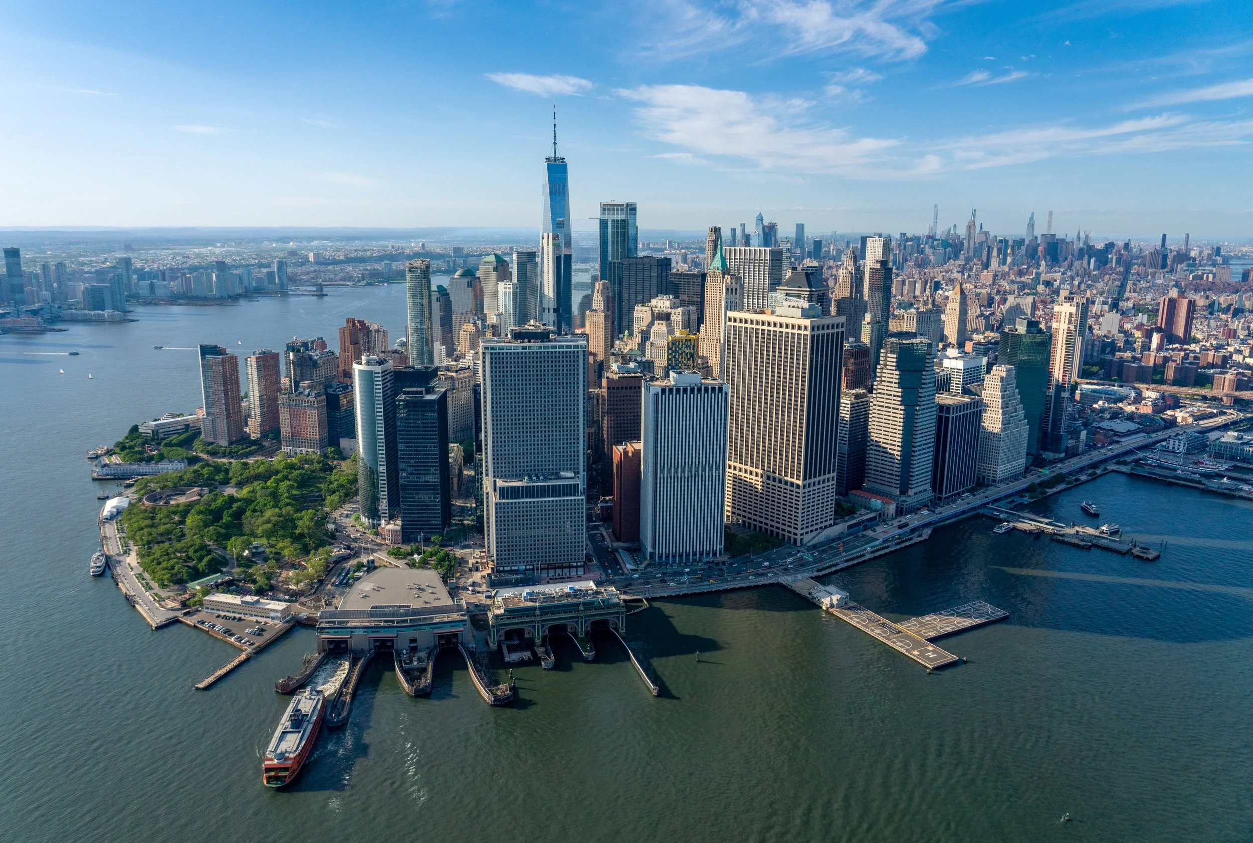 The Tip of Manhattan
A sweeping aerial view looking south over the Financial District. The shot captures the dense cluster of skyscrapers at the island's tip, with the Hudson and East Rivers converging. The scale of the city is emphasized by the tiny