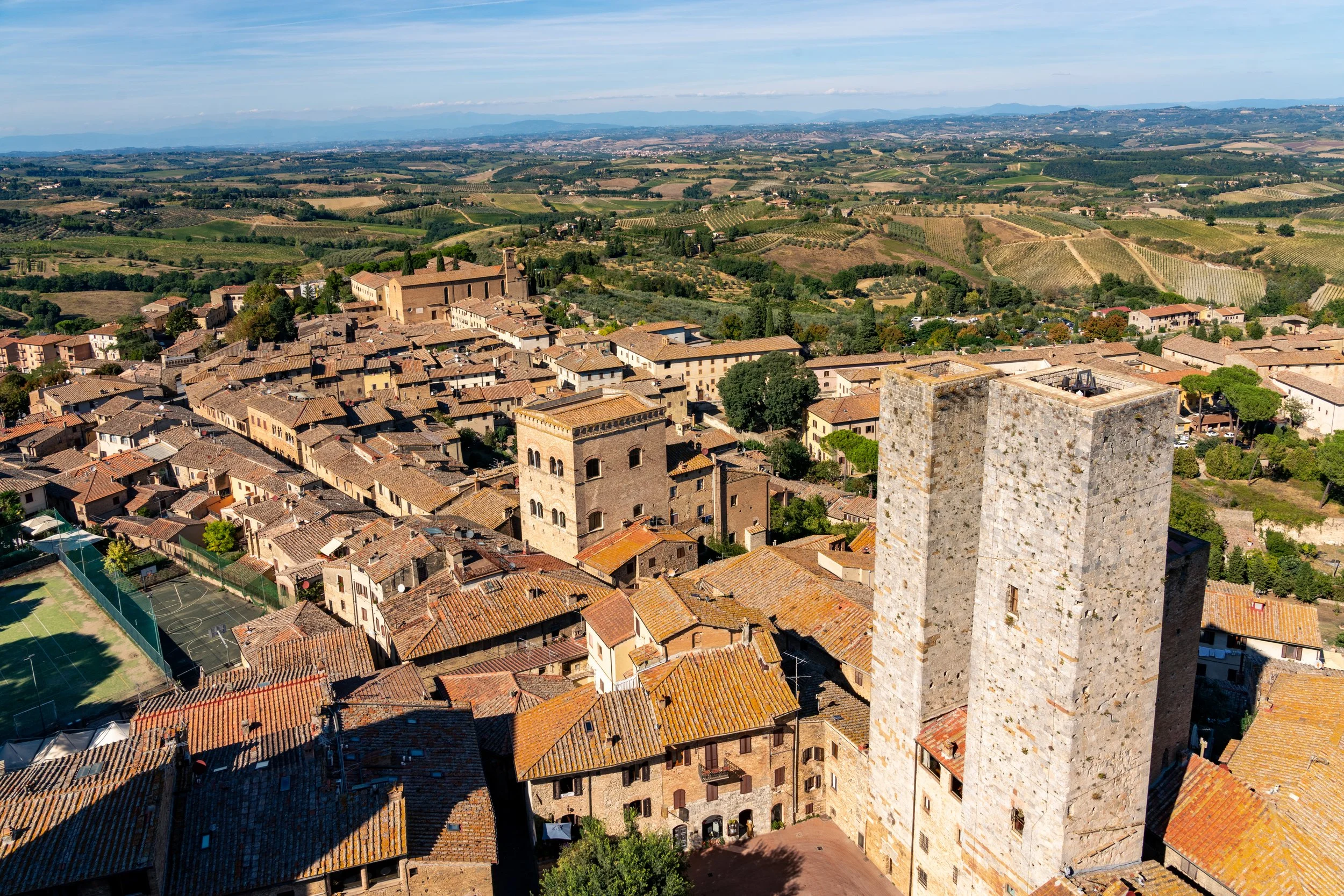Towers of Tuscany
A high-altitude perspective looking over the medieval hill town of San Gimignano. The shot captures the iconic stone towers, including the Torre Grossa, rising above a sea of weathered rooftops. This view emphasizes the town’s uniqu