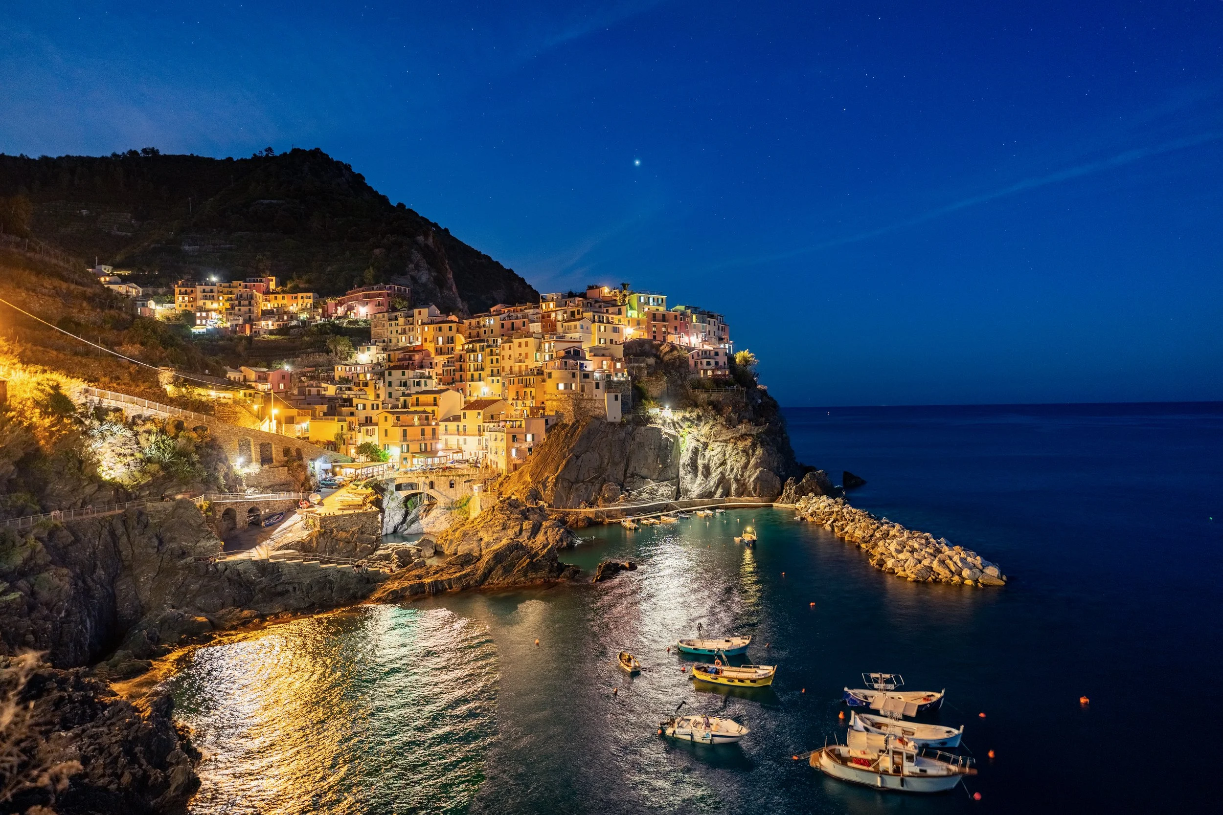 The Glowing Coast
The village of Vernazza in Cinque Terre clings to the rugged Italian cliffs, illuminated against the dark expanse of the Ligurian Sea. This long-exposure shot turns the crashing waves into a soft mist and brings out the brilliant te