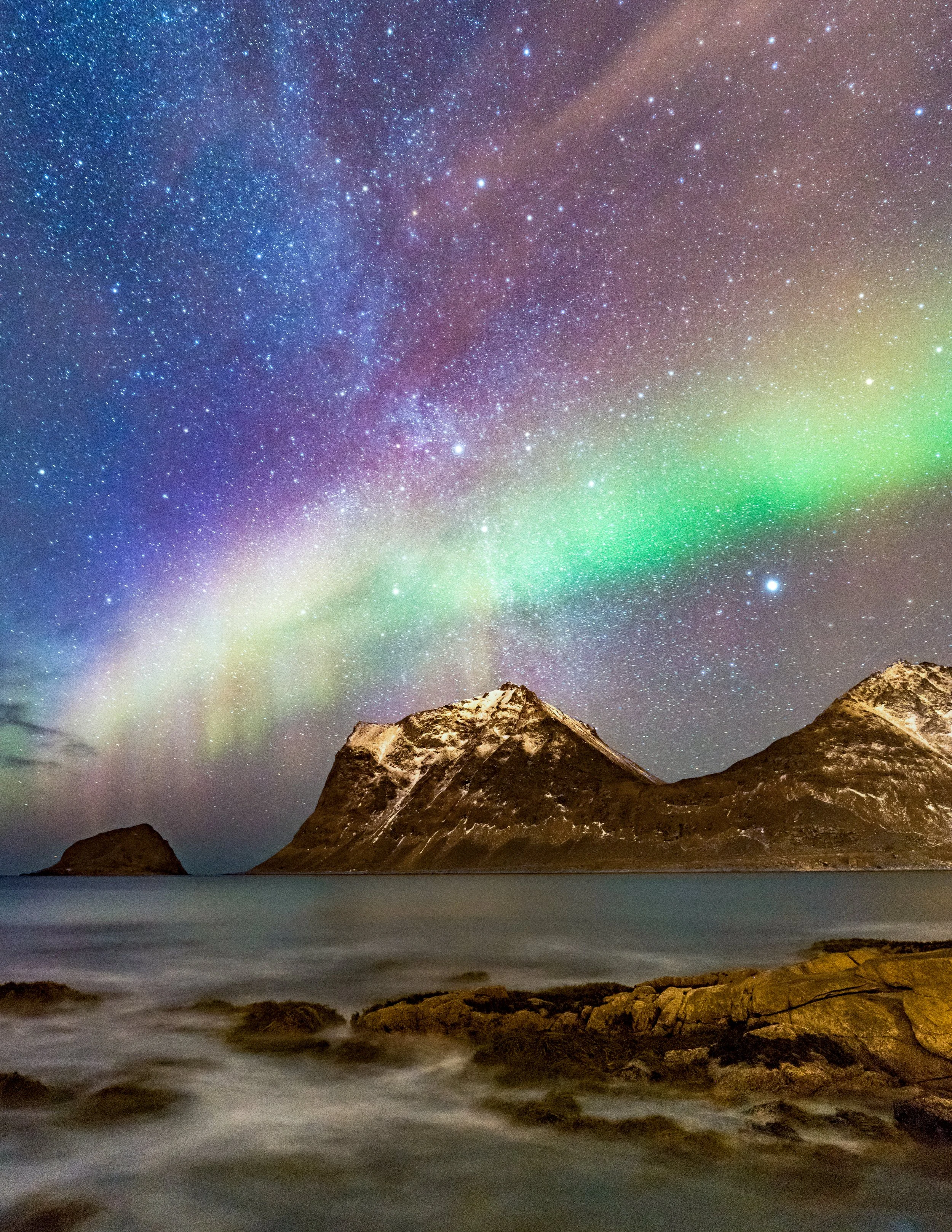 Arctic Radiance
A final, sweeping look at the Northern Lights as they stretch across the Lofoten Islands. This perspective emphasizes the scale of the mountains rising directly from the sea, with the green aurora acting as a bridge between the peaks 