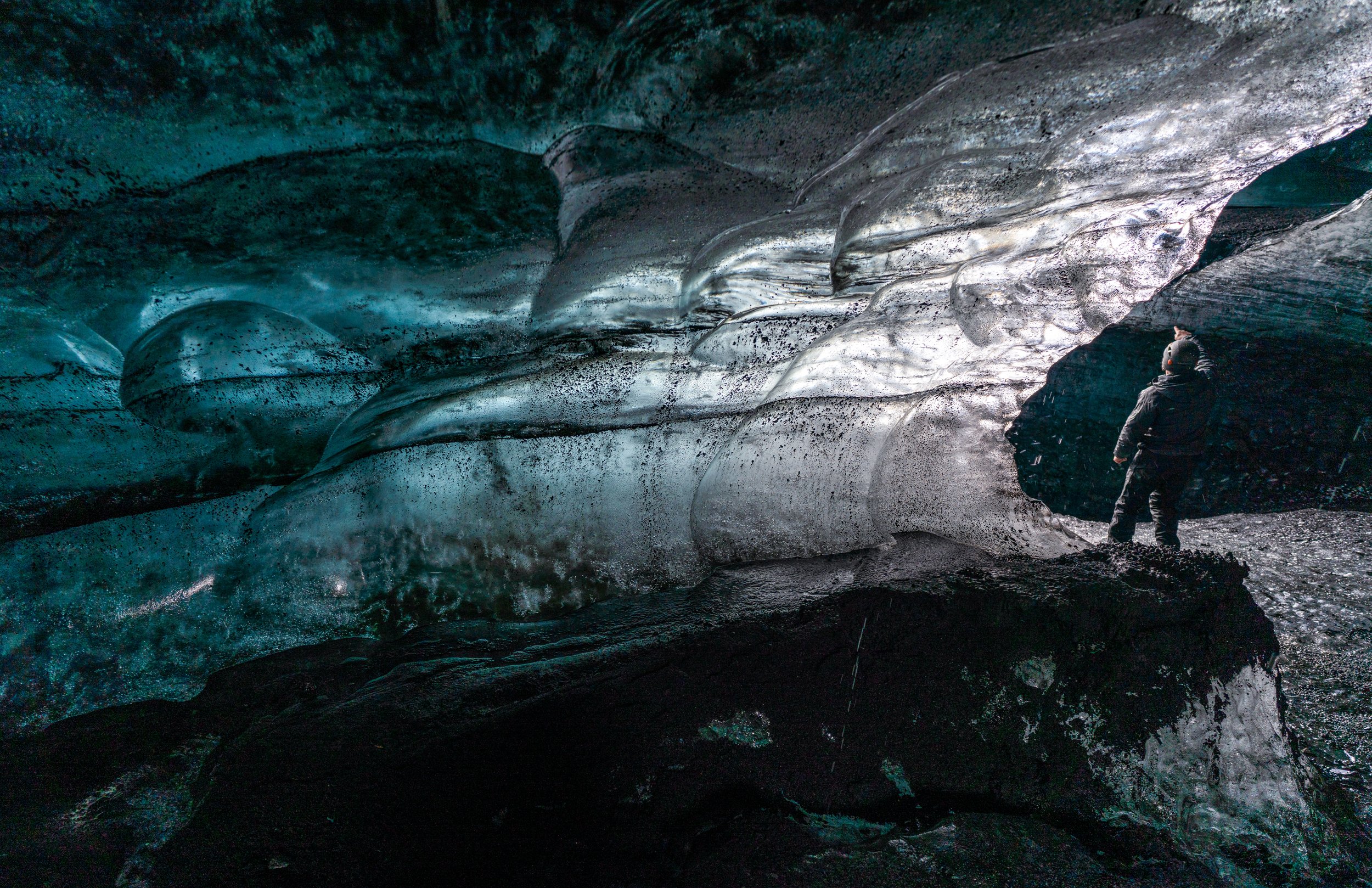 Standing in the Deep Blue
A lone explorer provides a sense of scale inside a massive ice cave beneath an Icelandic glacier. The scalloped walls are carved by air and water over centuries, creating a textured "golf ball" pattern that reflects light in