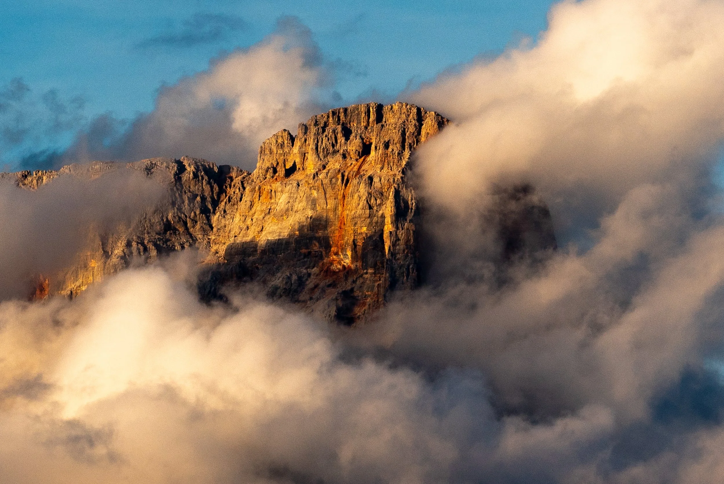 Golden Bastion
A dramatic view of a sun-drenched ridge within the Cinque Torri area. The warm light of the late afternoon catches the peaks of the rocks, contrasting sharply with the deep, cool shadows of the surrounding valleys. This shot highlights