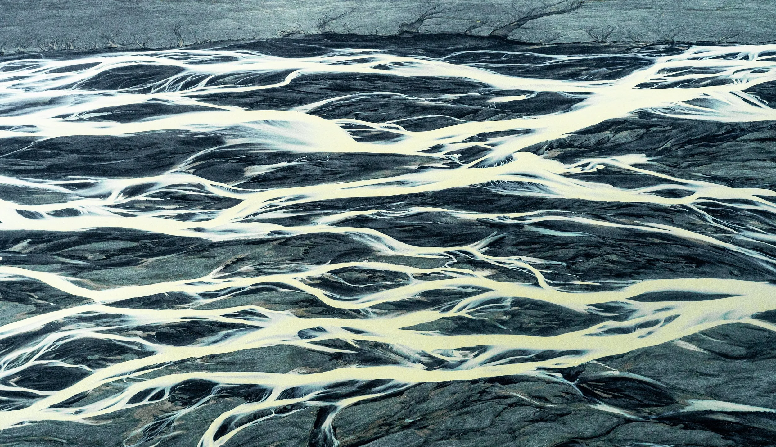 The Silver Vein
A stunning top-down view of a glacial river in Southern Iceland. The milky-white meltwater, rich with fine rock flour, carves a high-contrast path through the black volcanic sediment. From this altitude, the river looks less like wate