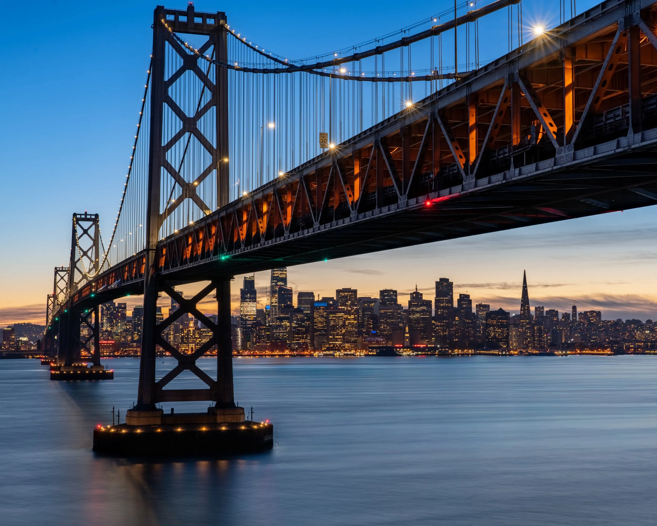 Across The Bay
An early evening view of the Bay Bridge stretching from the Yerba Buena Island toward the San Francisco skyline. While often overshadowed by its orange neighbor to the west, the Bay Bridge is a marvel of engineering, carrying over 260,