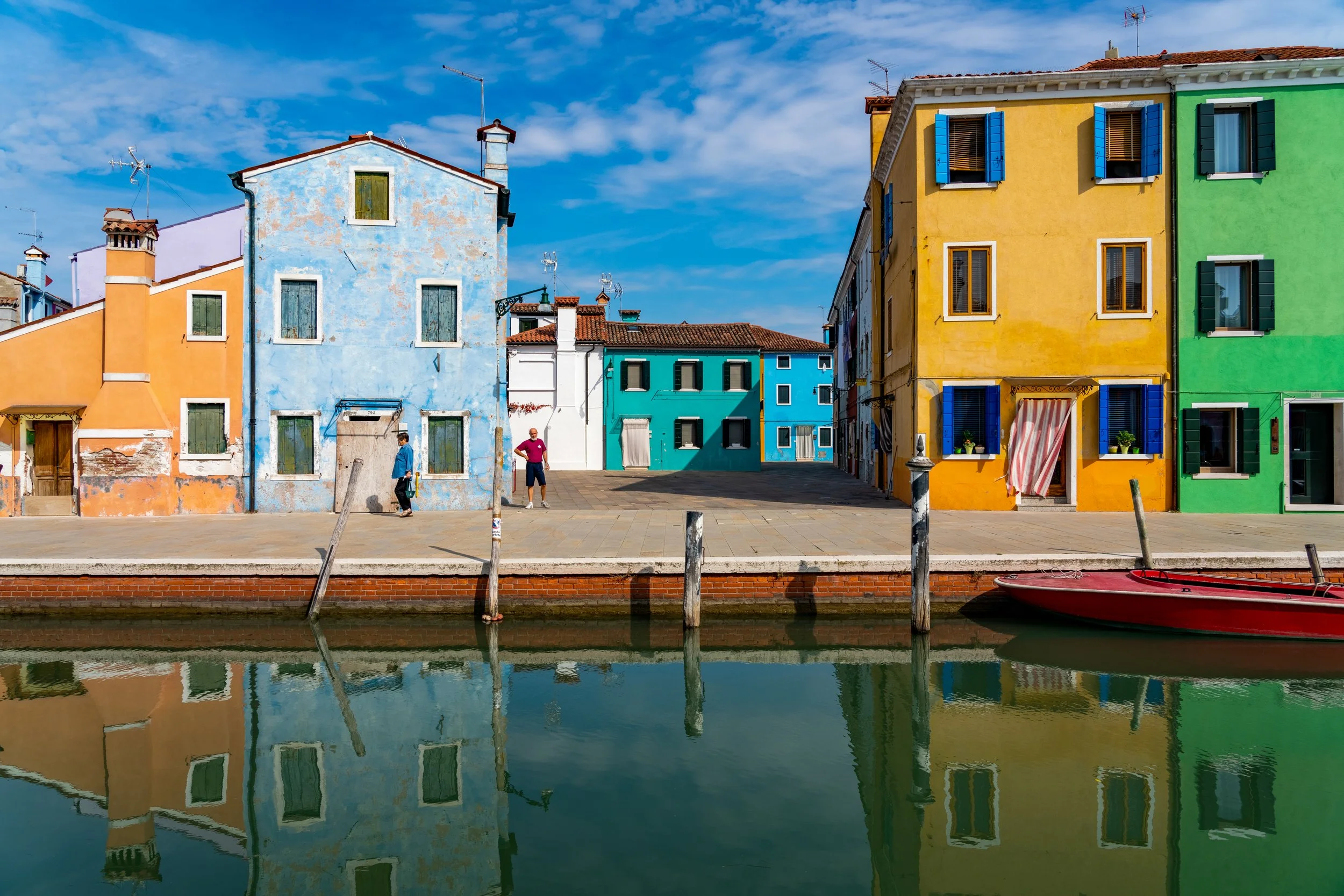 The Palette of Burano
A vibrant, cheerful perspective of the famously colorful homes lining the canals of Burano. The shot focuses on the reflection of the bright pink, blue, and yellow facades in the still water of the canal, capturing the unique is