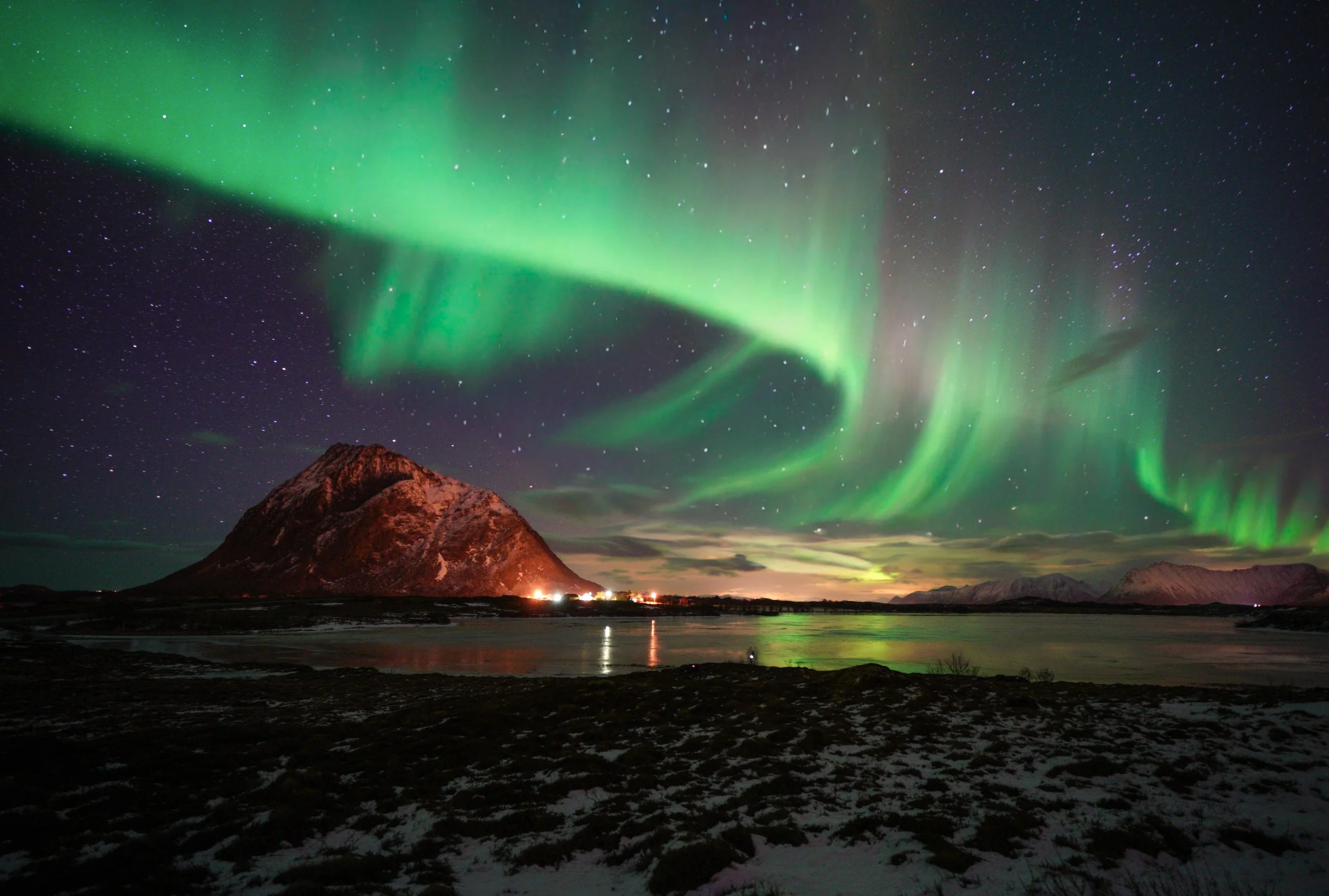 Arctic Emerald
A striking display of the Aurora Borealis flies over a jagged peak in Norway's Lofoten Islands. The intense green light of the aurora reflects off the snow-dusted slopes and the frozen waters below. This shot captures the raw, dramatic