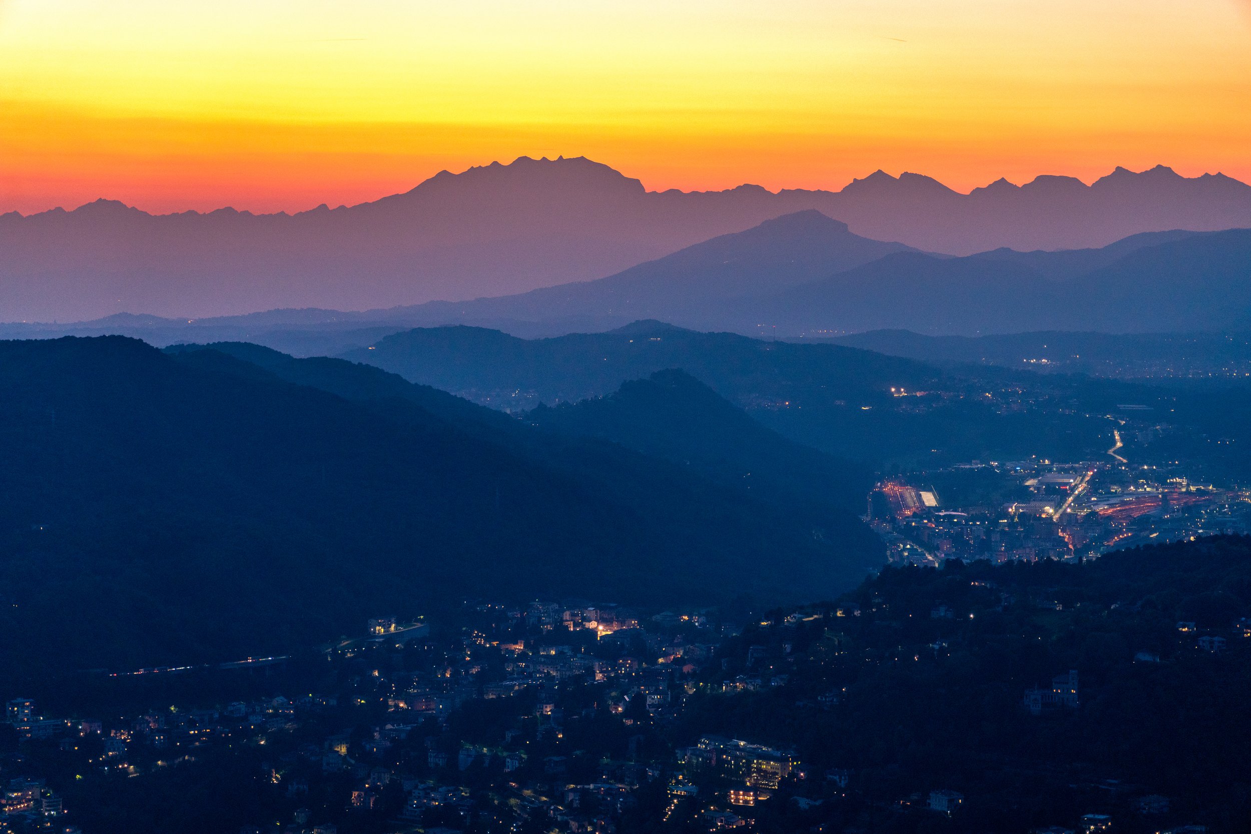 Mountain Ridges
A compressed, telephoto view of distant mountain ridges fading into the sunset. The fading light creates striking, atmospheric layers of deep blue and purple silhouettes against a vibrant orange and yellow horizon. It’s a serene, pain