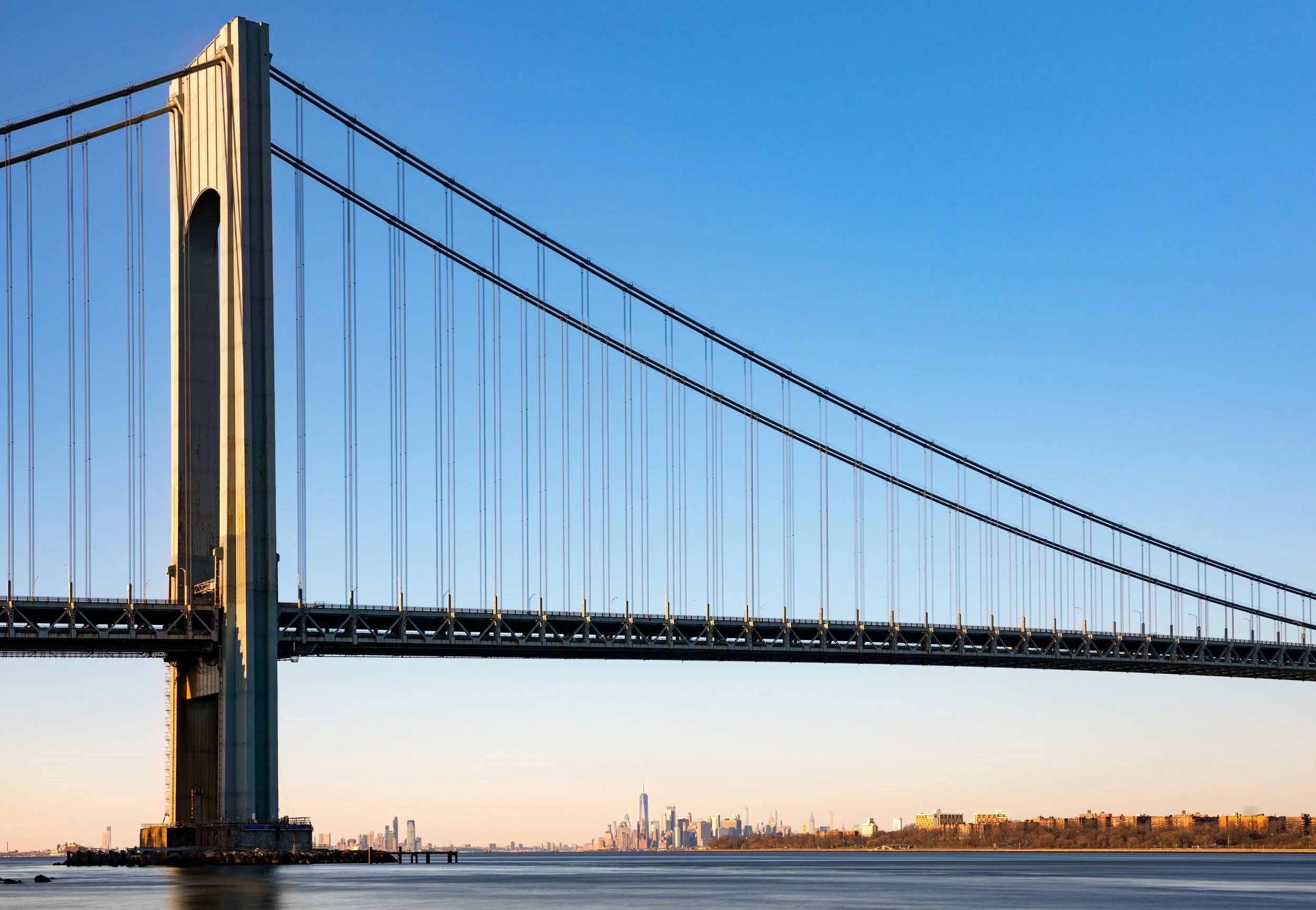 The Gateway to the Atlantic
Looking out from the shores of Staten Island, the Verrazzano-Narrows Bridge stretches across the water toward Brooklyn. This wide-angle shot captures the massive scale of the suspension bridge against a dramatic sky, with 