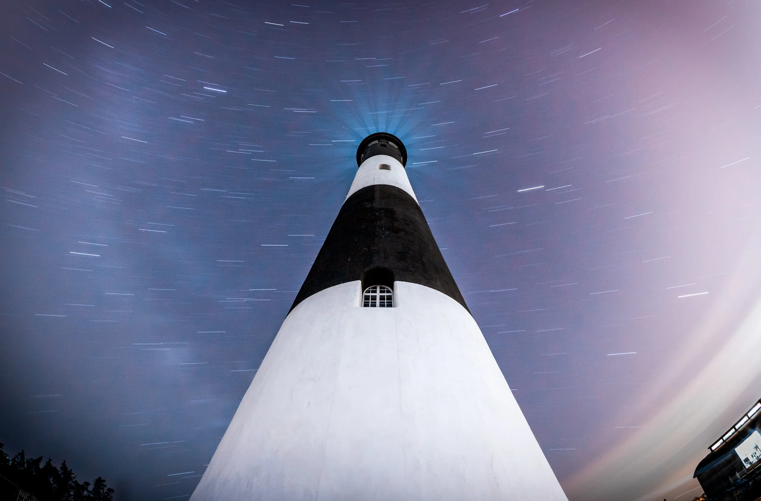Star Trails Over Fire Island
A dramatic low-angle perspective of the Fire Island Lighthouse under a swirling night sky. By using a long exposure, the earth’s rotation is captured as circular star trails centered around Polaris. The stark black-and-wh