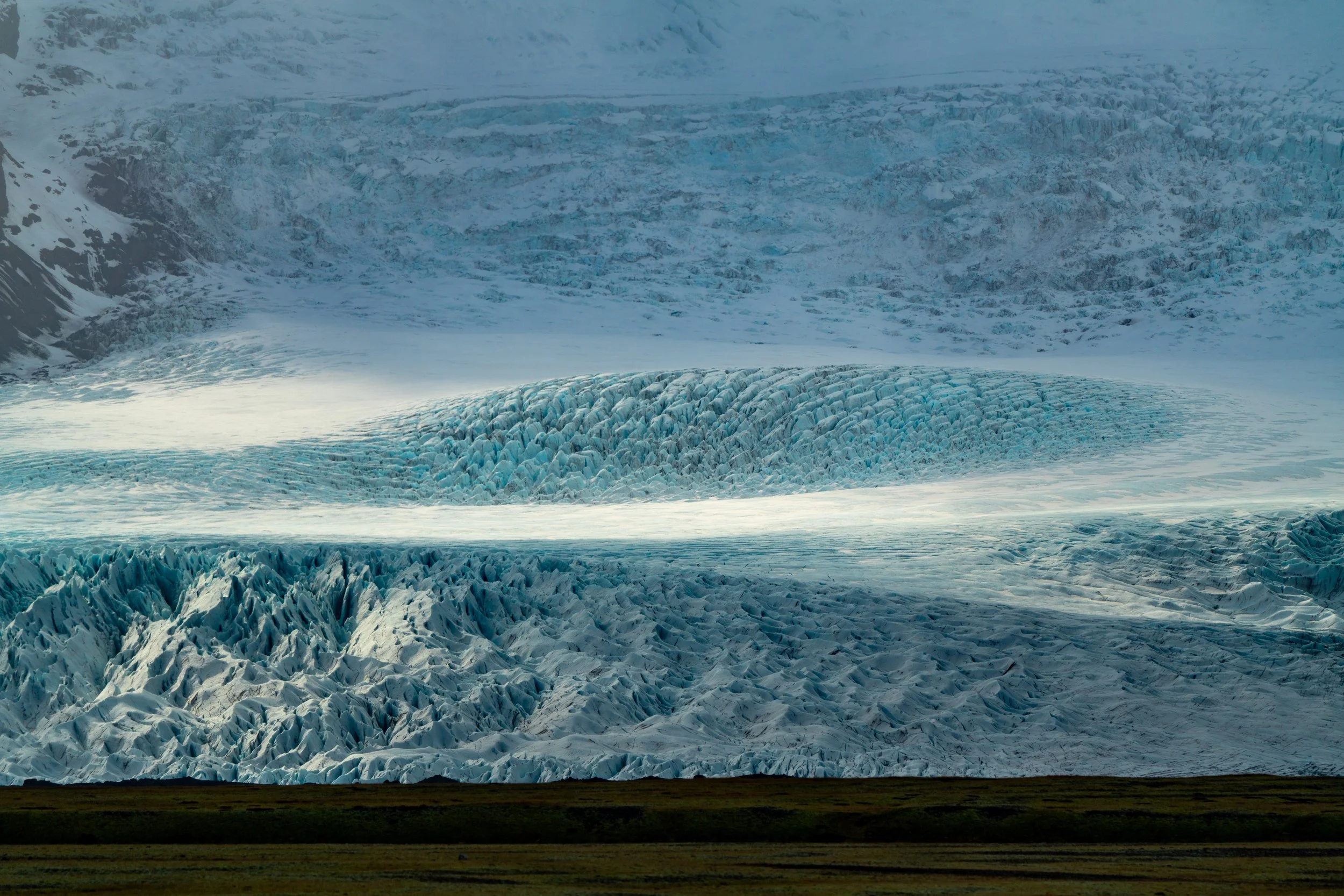 The Edge of the Ice Cap
A sweeping view of a glacial tongue as it descends from the Vatnajökull ice cap. The deep blue fissures and crevasses visible in the ice are the result of immense pressure and the slow, relentless movement of the glacier over 