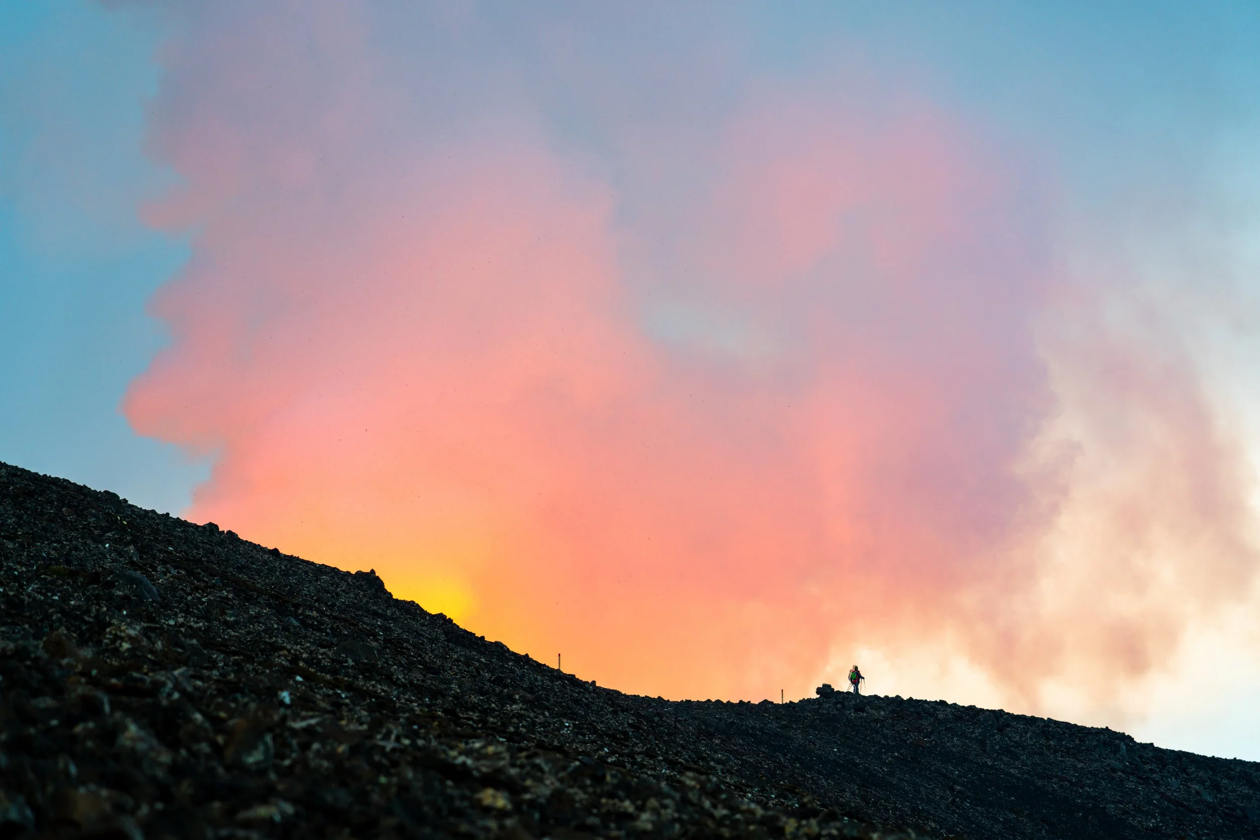 A Witness to Creation
A lone figure stands on the ridge as the sky glows with the reflection of the Fagradalsfjall Volcano. This shot provides a rare sense of scale, contrasting the smallness of man against the monumental birth of new land. The haze 