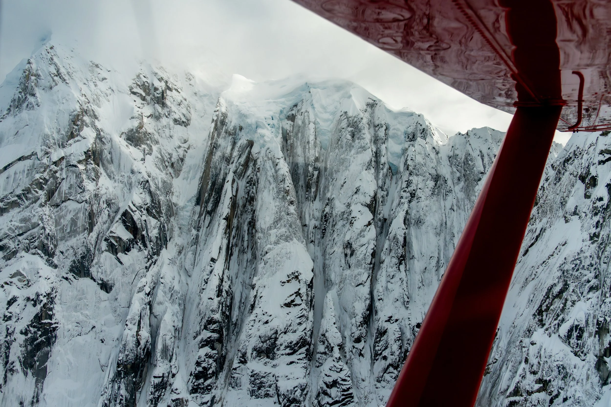 The Pilot’s View
A rare perspective of the Alaska Range framed by the structural lines of a plane's window. This shot provides a sense of the scale and isolation of the high-altitude wilderness, placing the viewer directly in the seat of the explorer